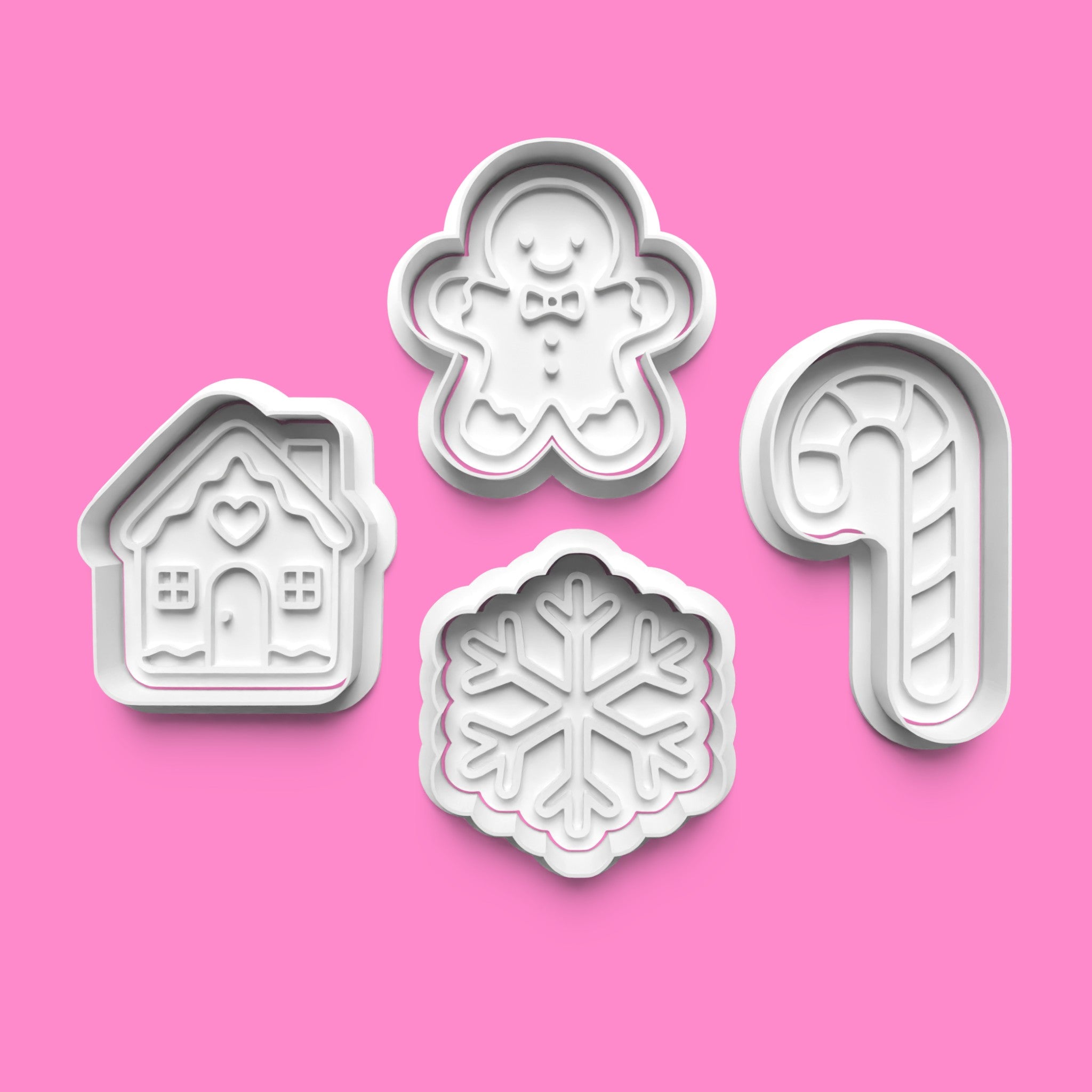 Set of four cookie cutters shaped like a gingerbread man, house, snowflake, and candy cane on a pink background.