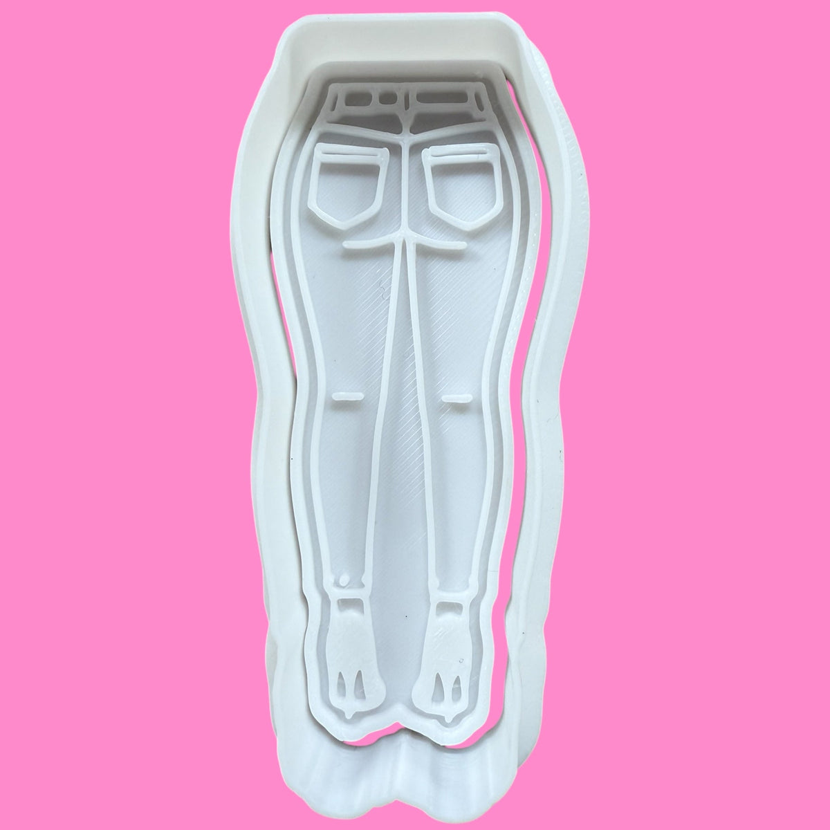 A plastic cookie cutter and embosser in the shape of flared jeans and high heels, designed for fashion-themed baking.