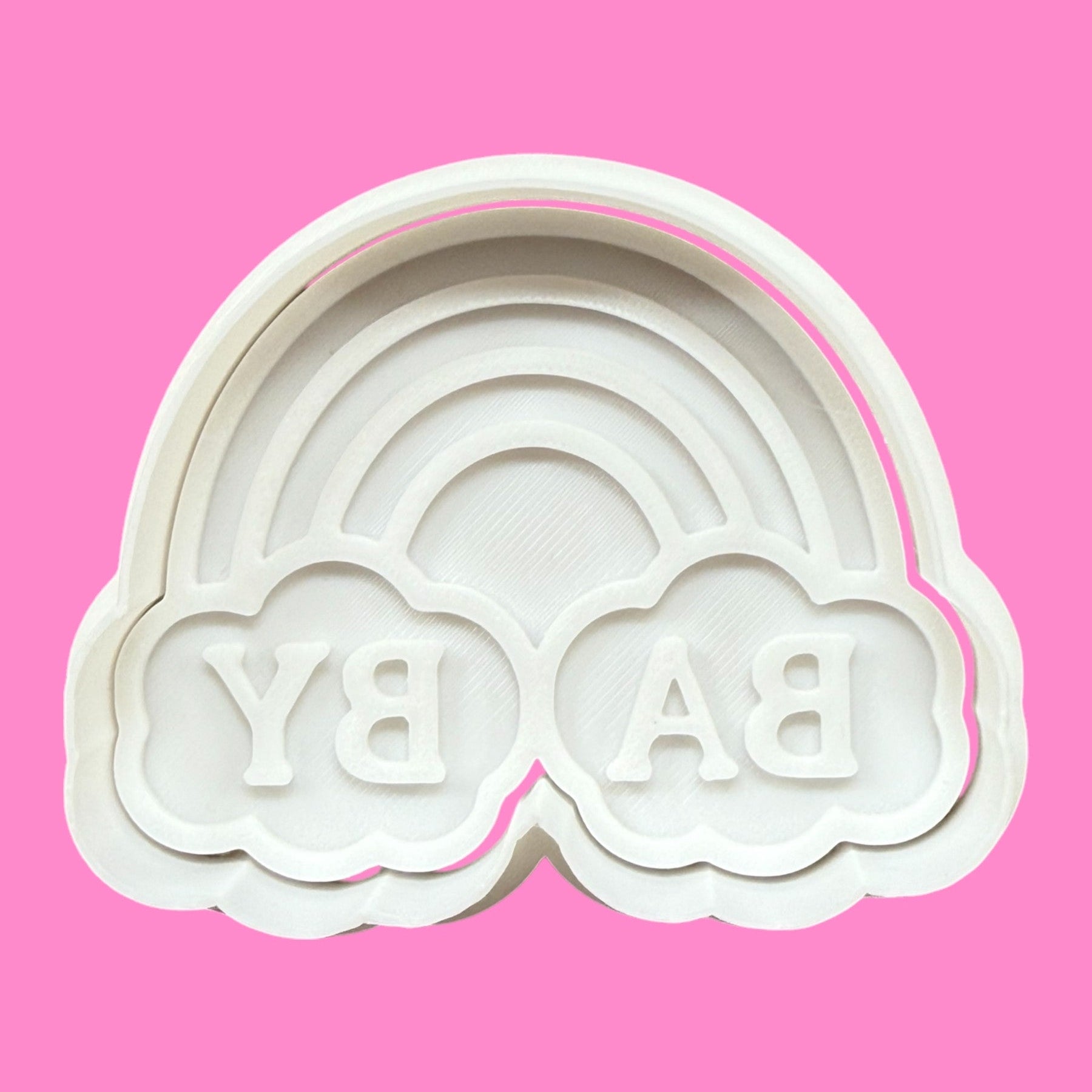 A plastic cookie cutter and embosser mold in the shape of a cloud with a rainbow arch and the words 'BYE BABY' embossed on it against a pink background.