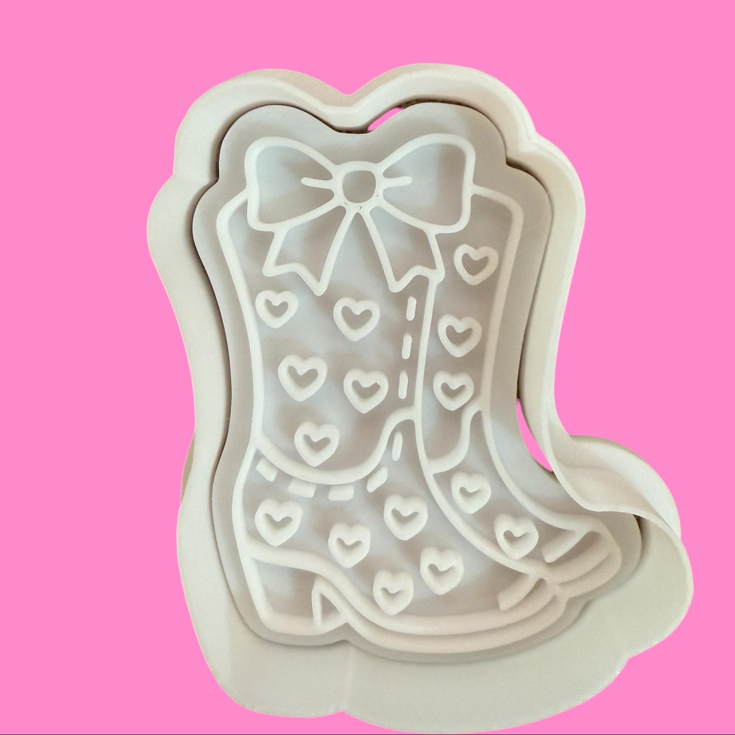 A cookie cutter and embosser set in the shape of a cowboy boot with a ribbon detail.