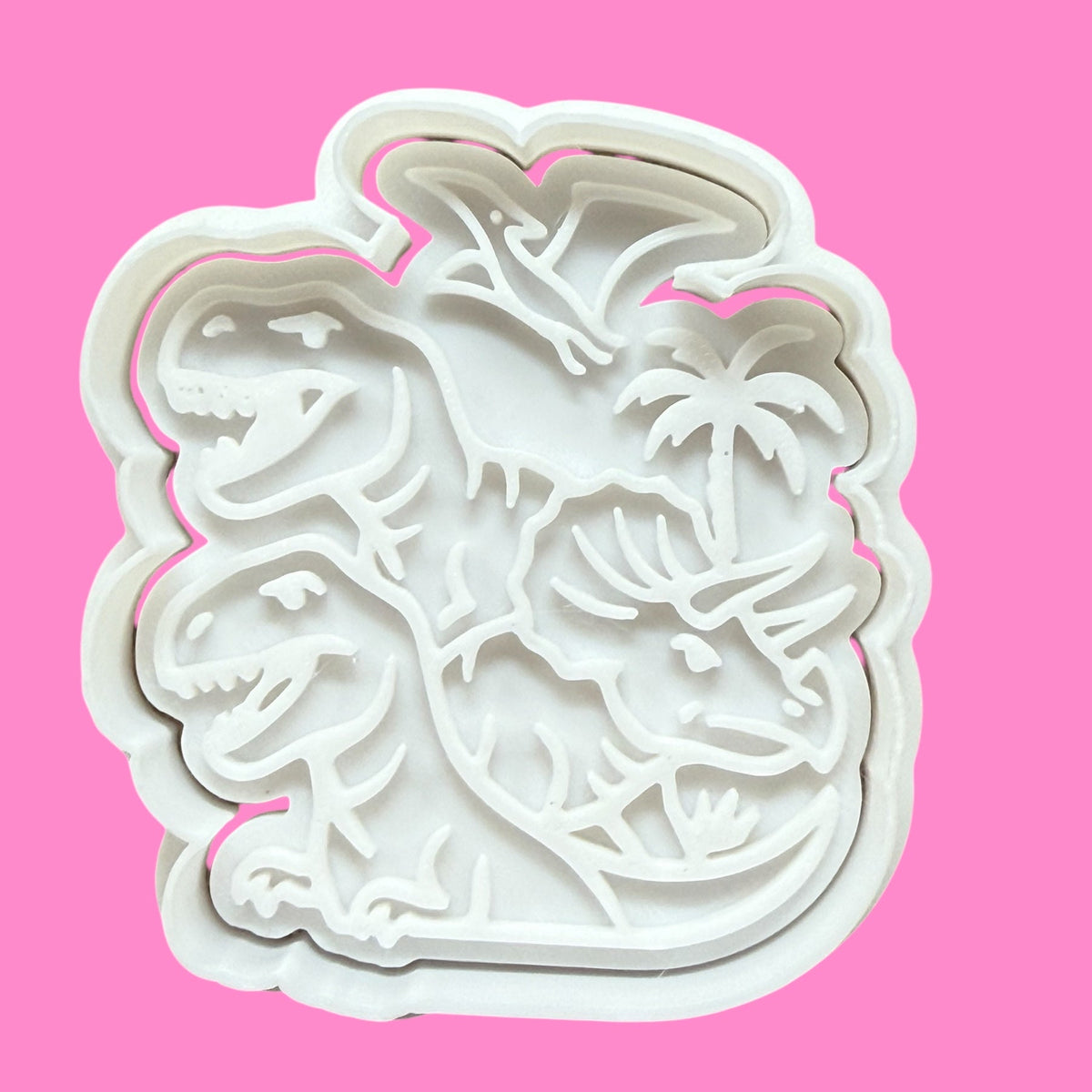 A white plastic dinosaur-shaped cookie cutter and embosser against a pink background.