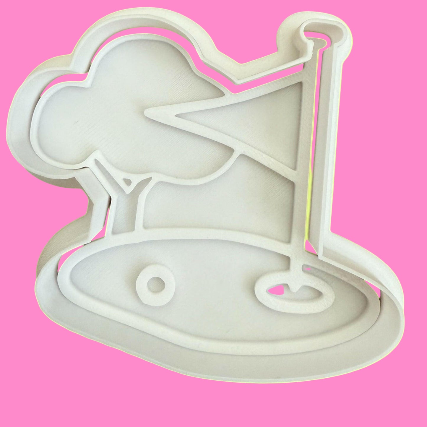 A plastic cookie cutter and stamp set with a design of a golf green including a tree, ball, and flag.