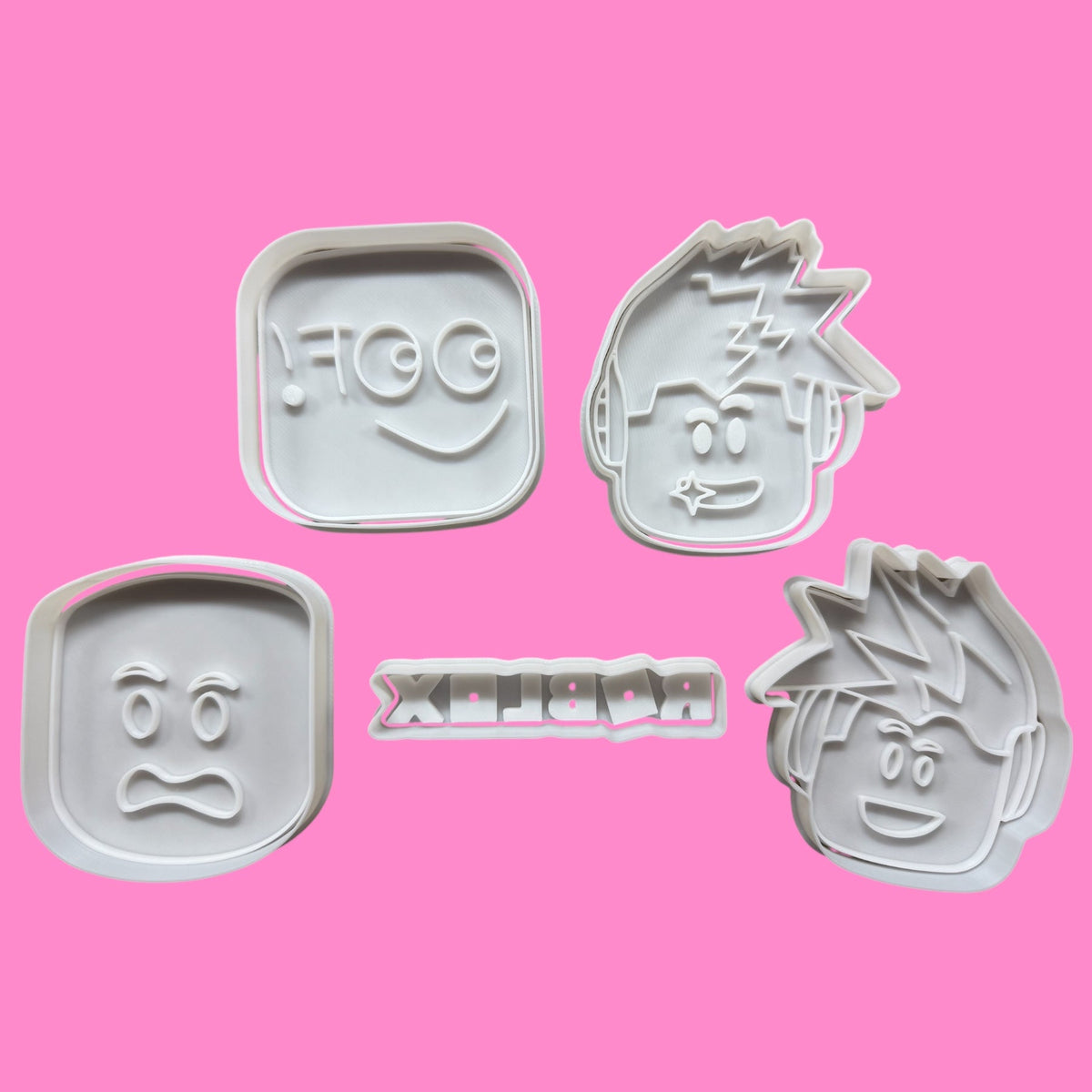 A collection of five Roblox-inspired cookie cutters and embossers, featuring the iconic logo and four character designs, placed against a pink background.
