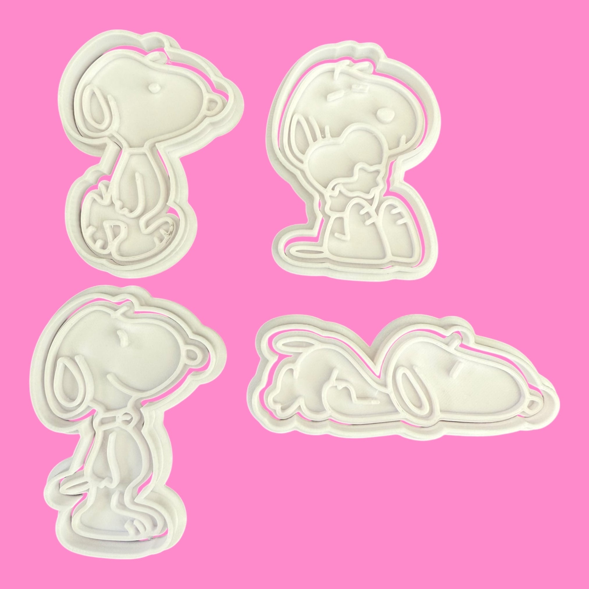 Four white cookie cutters shaped like cartoon characters on a pink background