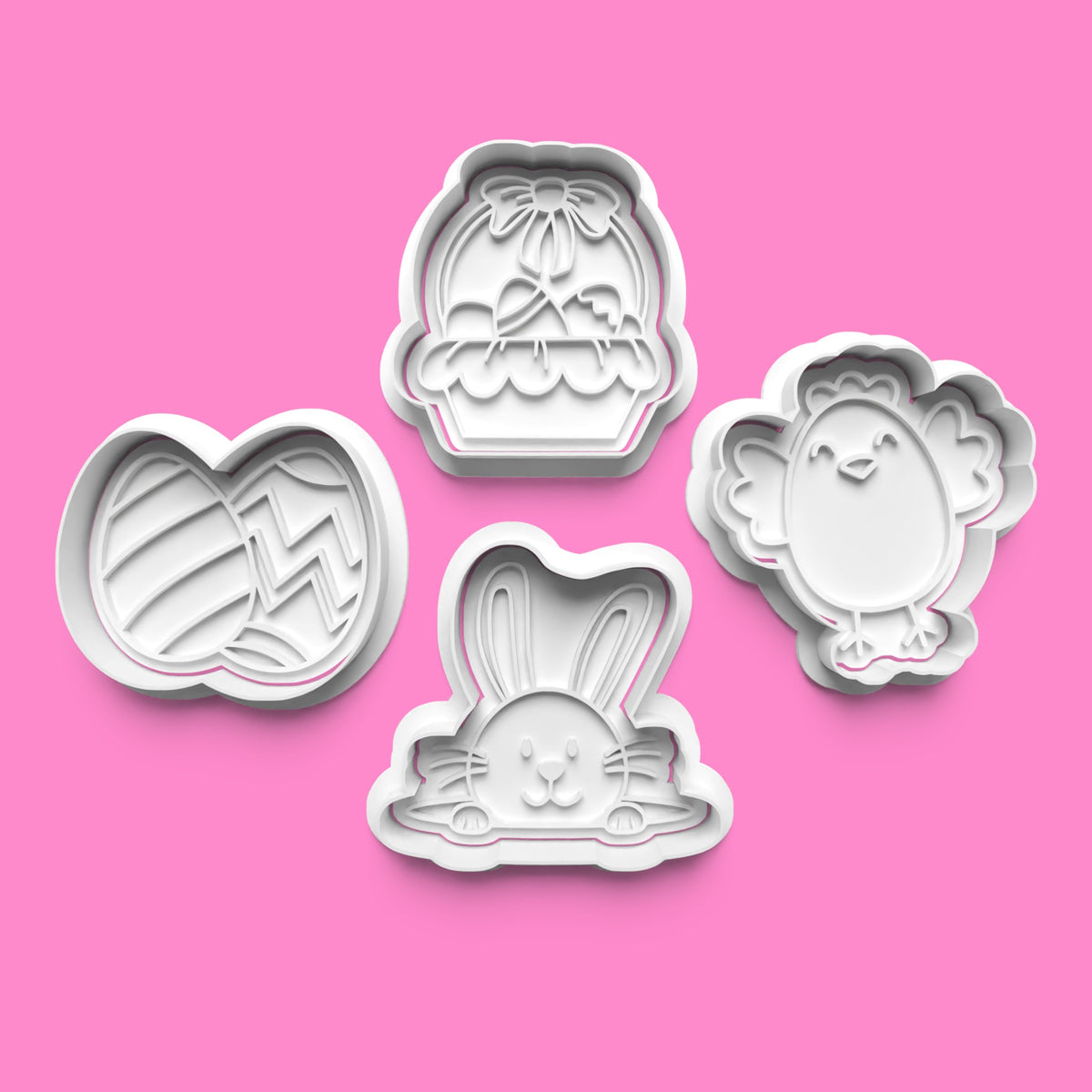 A set of four white Easter-themed cookie cutters and stamps, including designs for a bunny, a chick, an egg, and a basket, displayed on a pink background.