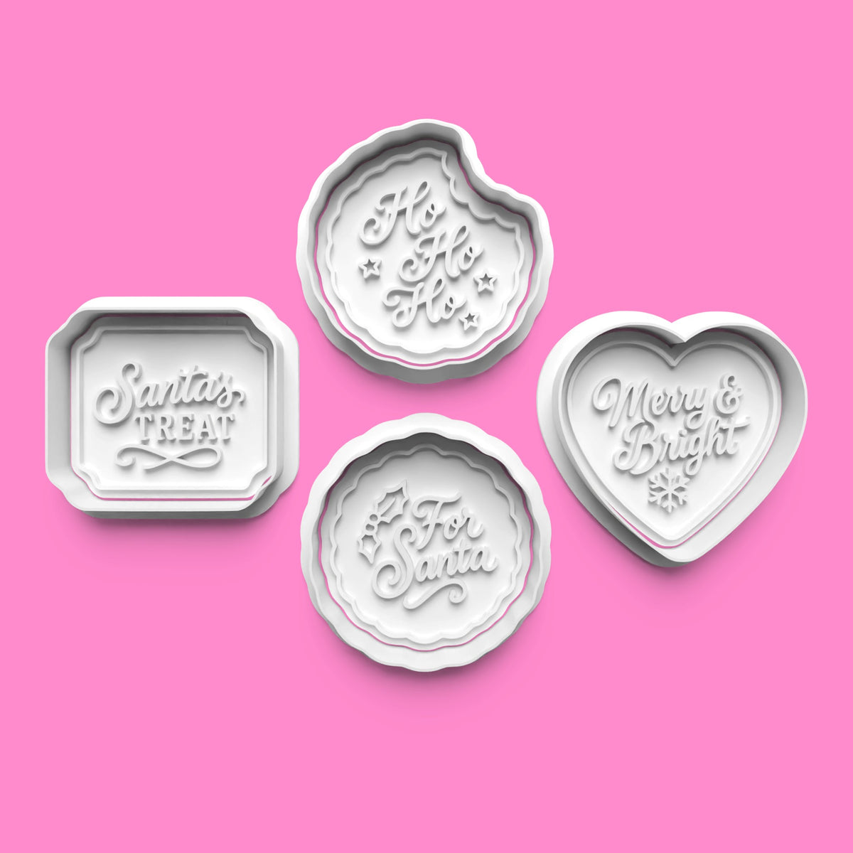 Four white embossed cookie cutters or stamps in different holiday shapes, including a rectangular one reading 'Santa's Treat,' a heart-shaped one reading 'Merry & Bright,' and two round ones reading 'Ho Ho Ho' and 'For Santa,' arranged on a solid pink background.