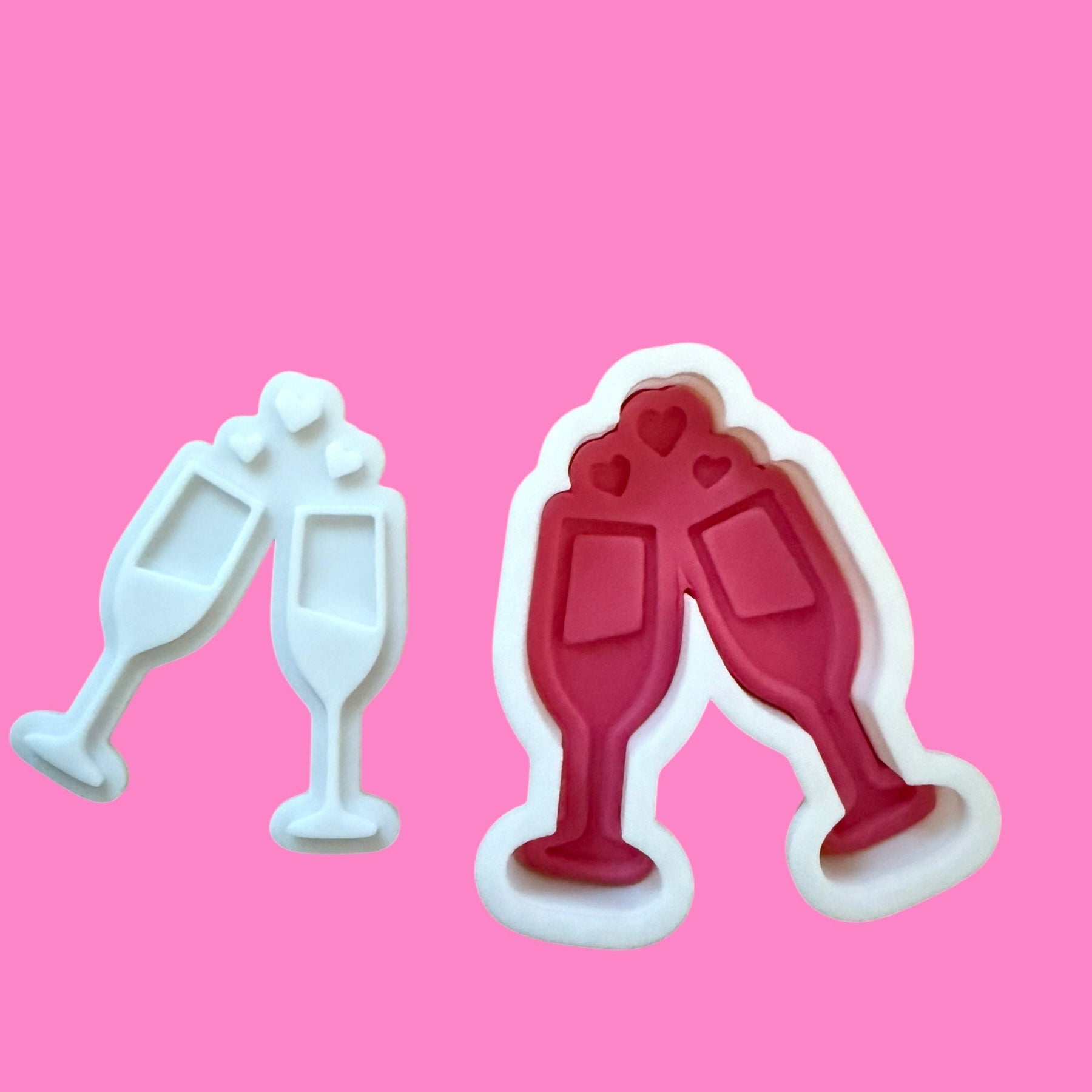 Two cookie cutters shaped like champagne glasses on a pink background