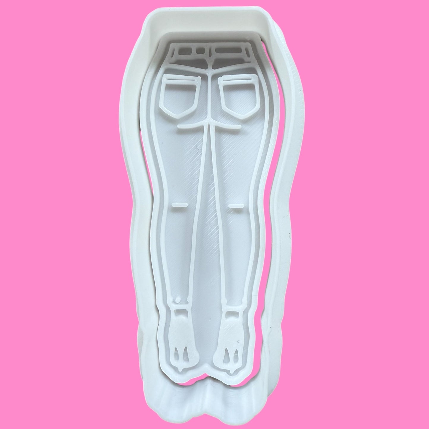A plastic cookie cutter and embosser in the shape of flared jeans and high heels, designed for fashion-themed baking.