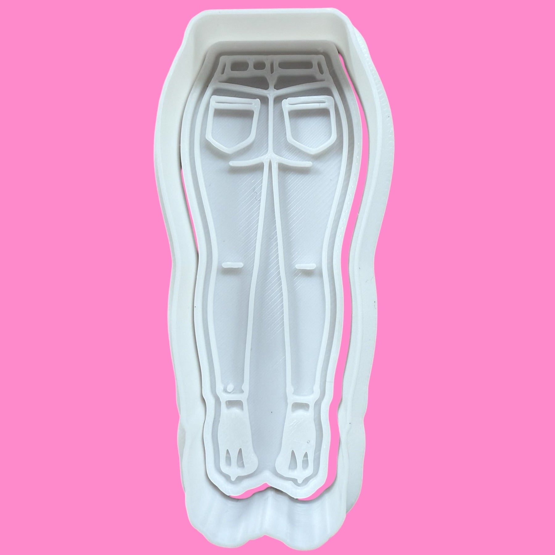 A plastic cookie cutter and embosser in the shape of flared jeans and high heels, designed for fashion-themed baking.