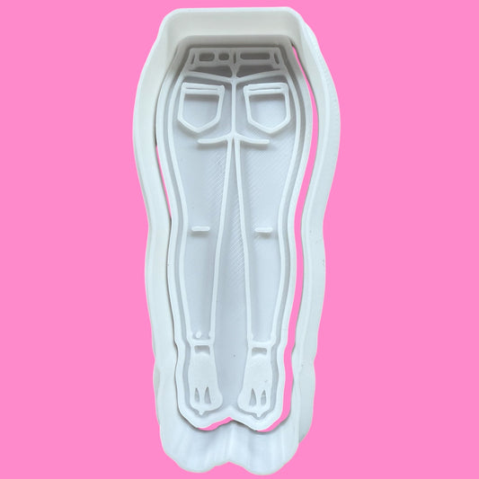 A plastic cookie cutter and embosser in the shape of flared jeans and high heels, designed for fashion-themed baking.