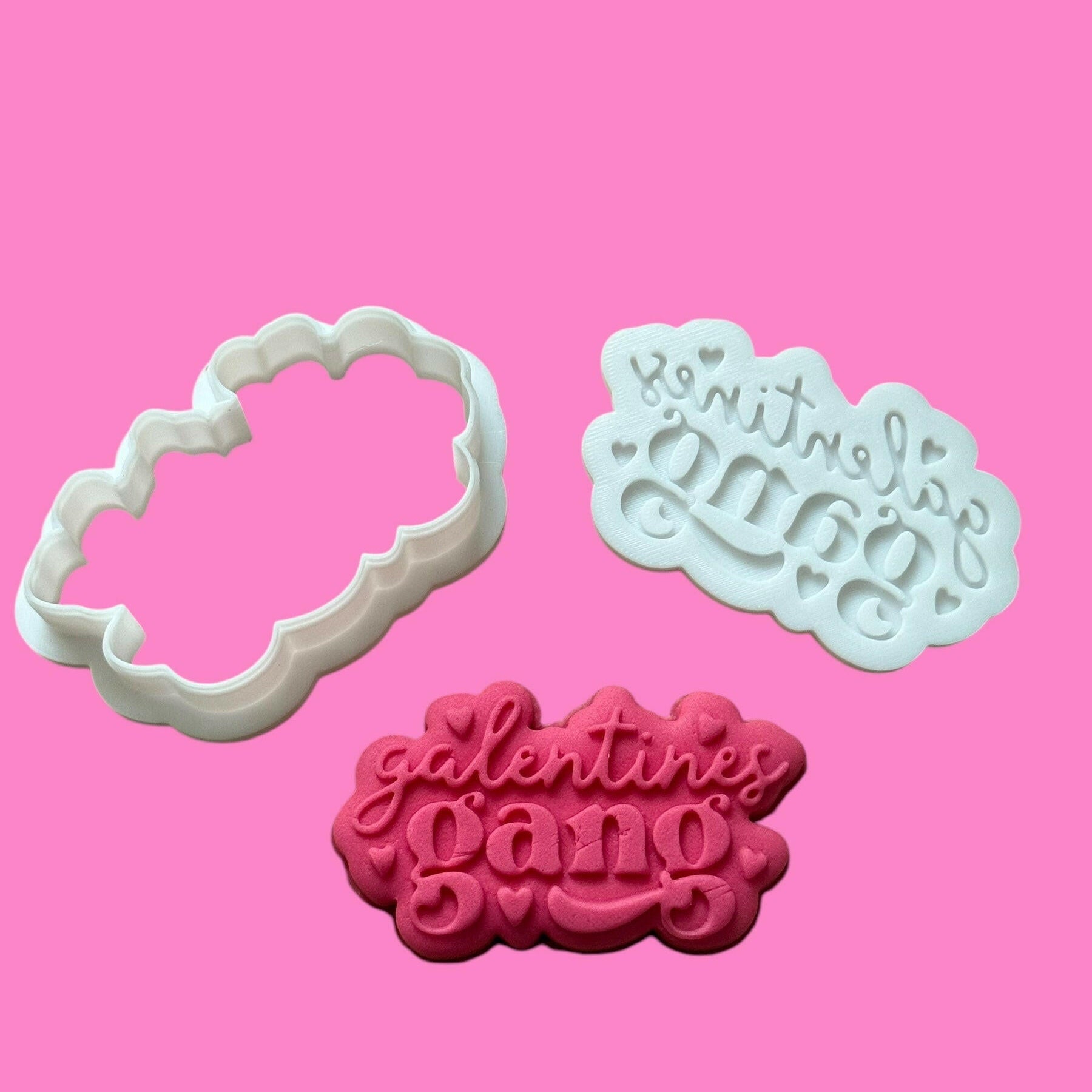 Two white cookie cutters with the phrase 'Galentines Gang' in a bold, trendy font, displayed on a pink background.