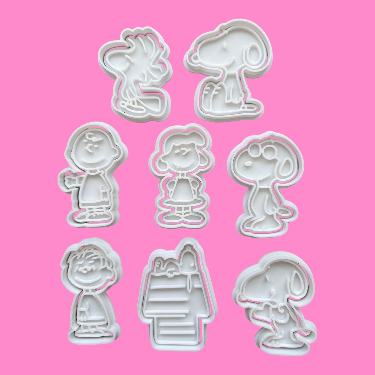 Set of eight cookie cutters shaped like cartoon characters on a pink background