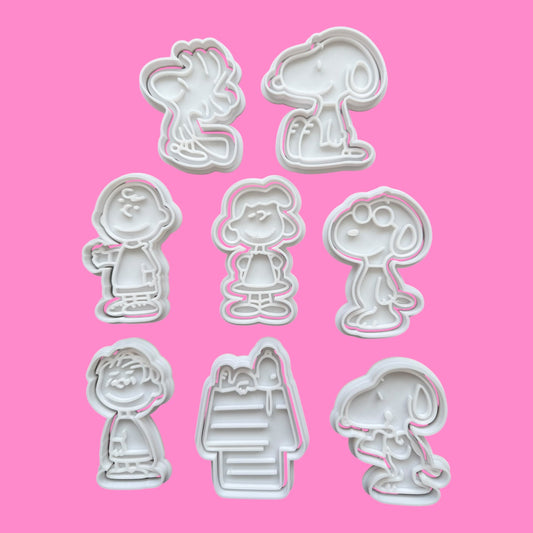 Set of eight cookie cutters shaped like cartoon characters on a pink background
