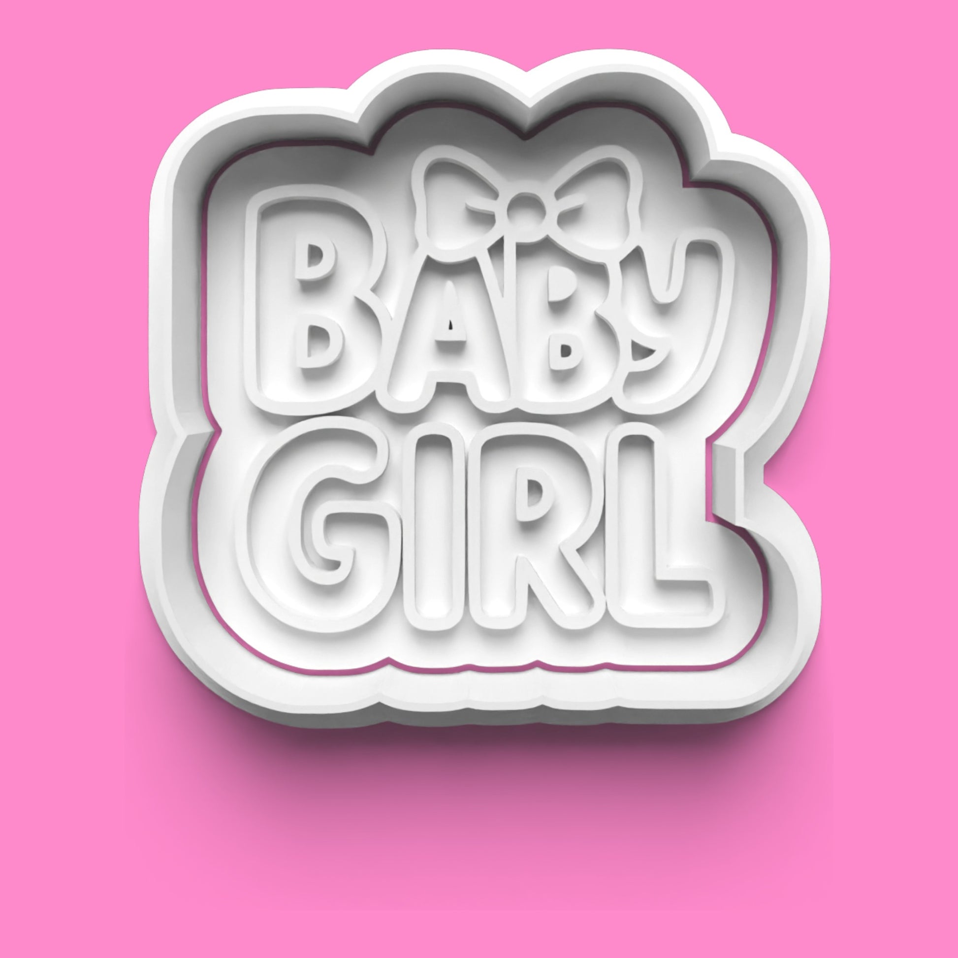 Cookie cutter with 'BABY GIRL' text and a bow on a pink background