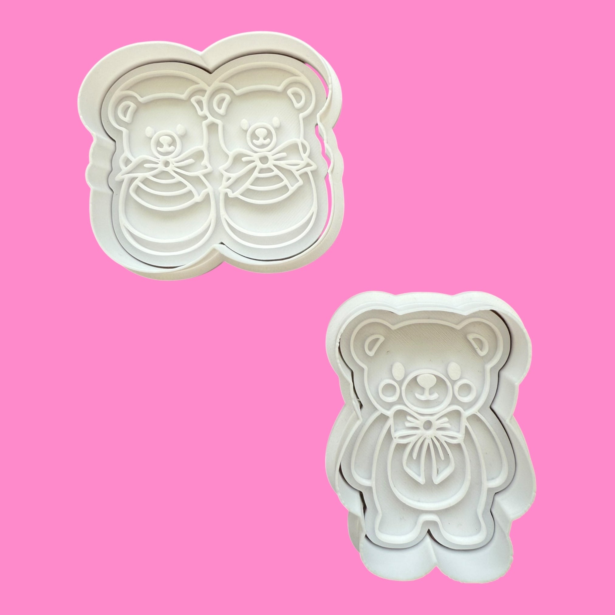 Two cookie cutters shaped like a teddy bear and a pair of shoes on a pink background