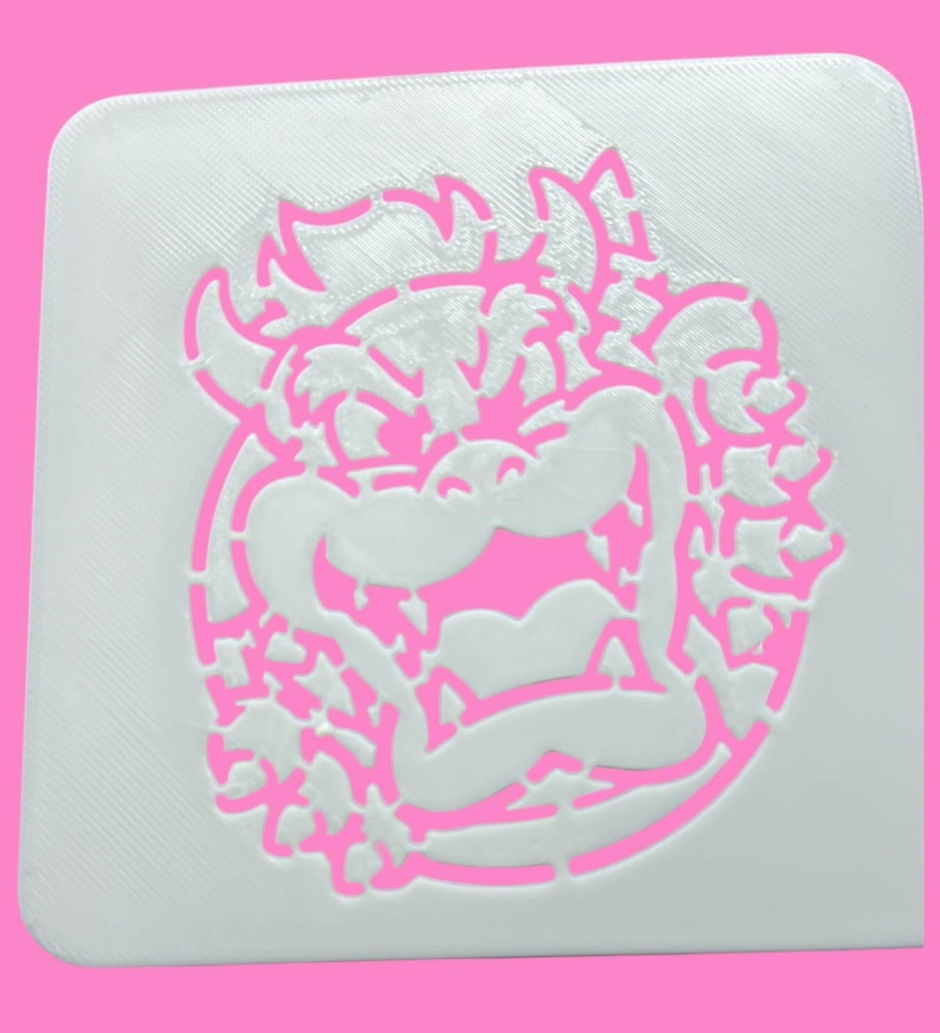 A white square food-safe PLA stencil with a pinkBowser-inspired design for cookie, cake, and fondant decorating.