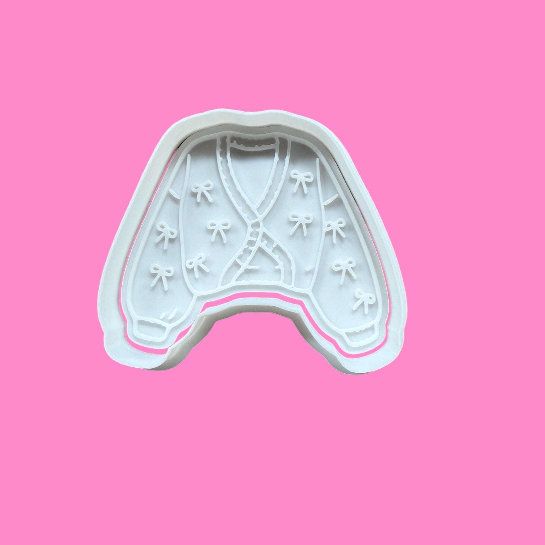 A cookie cutter and embosser with a cozy knit-inspired design, featuring cardigan texture with tied ribbon accents.