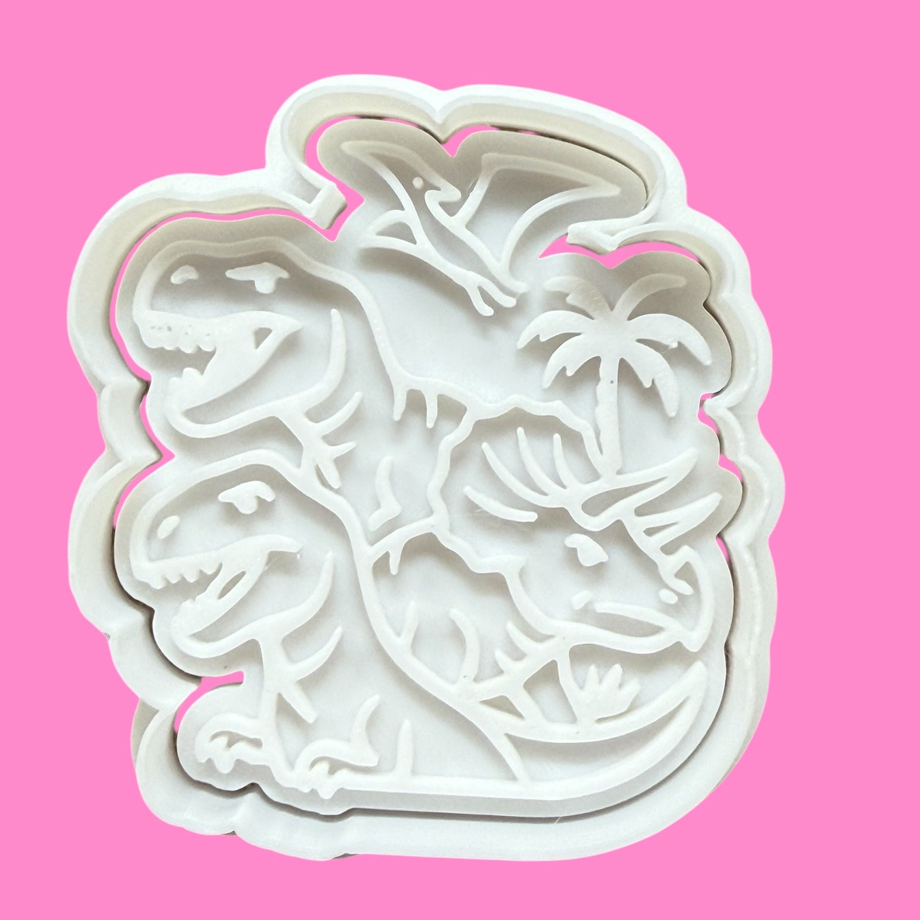 A white plastic dinosaur-shaped cookie cutter and embosser against a pink background.