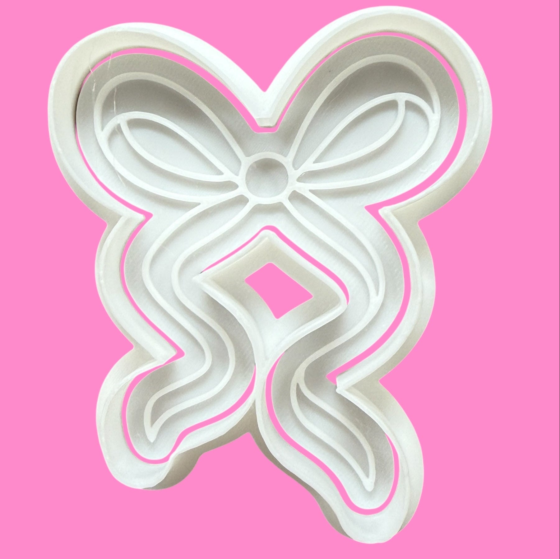 A white, elegant ribbon-shaped cookie cutter on a pink background.