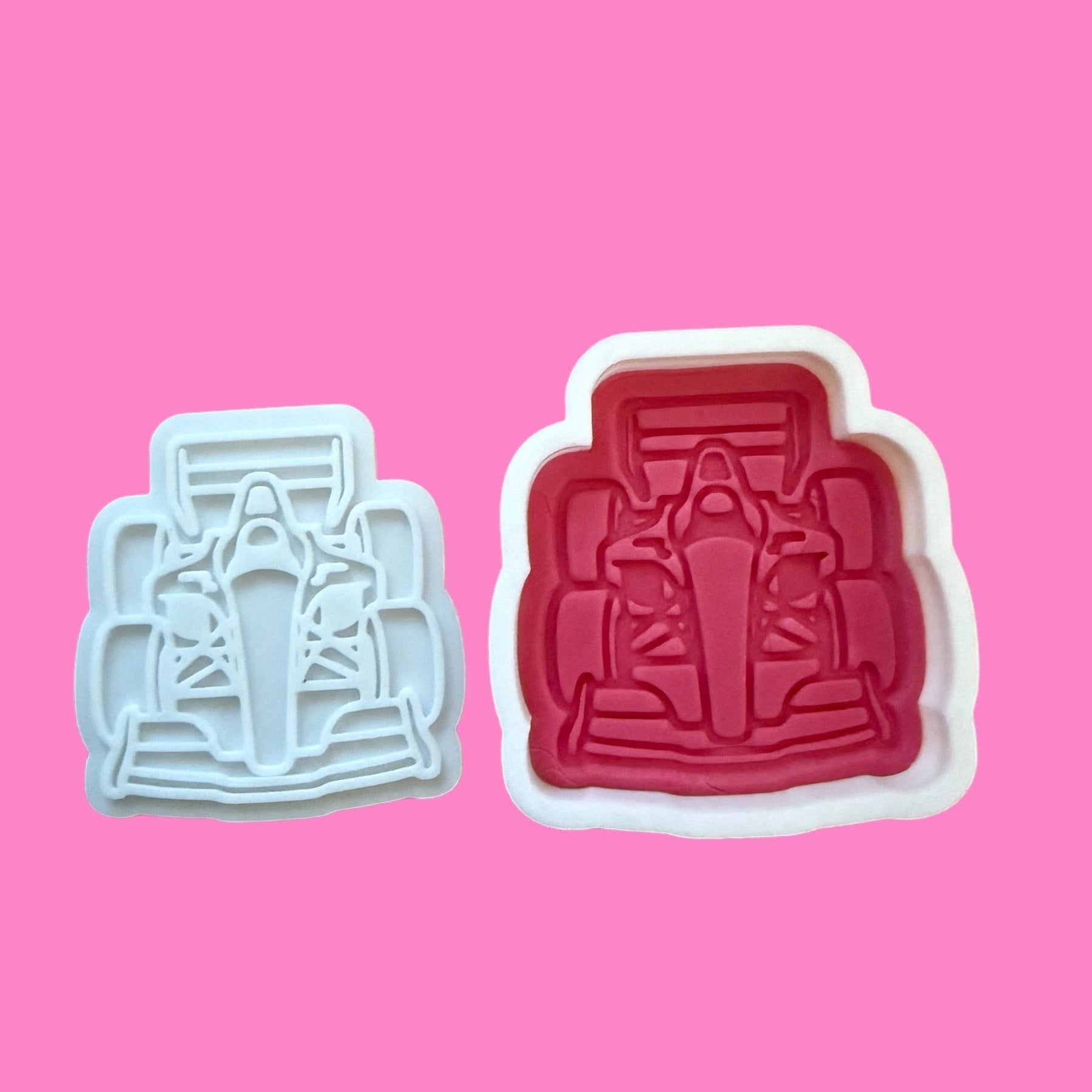 Two cookie cutters with Formula 1 racing-inspired designs. One cutter is white, and the other is red, embossed with details of a racing car.