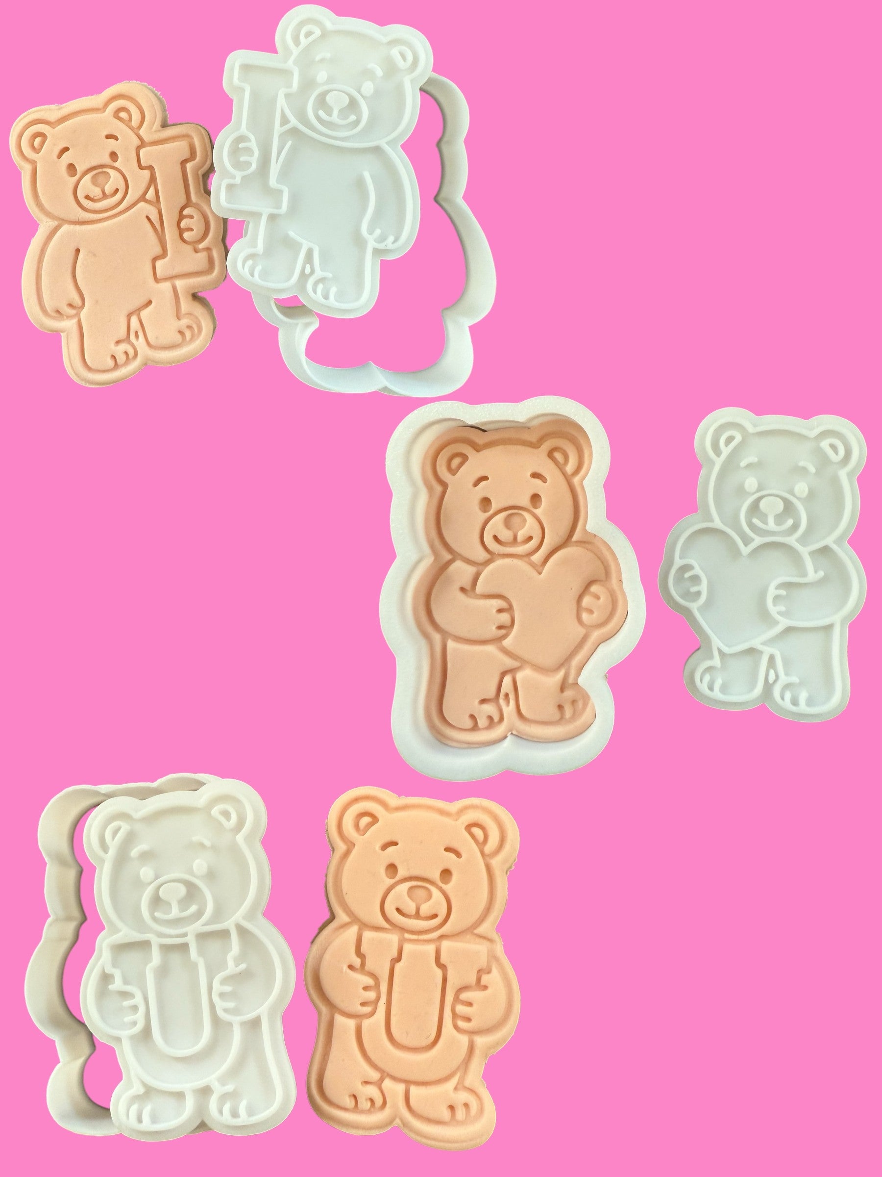 A set of three bear-shaped cookie cutters in different colors, each holding a letter: 'I', a heart, and 'U', against a pink background.
