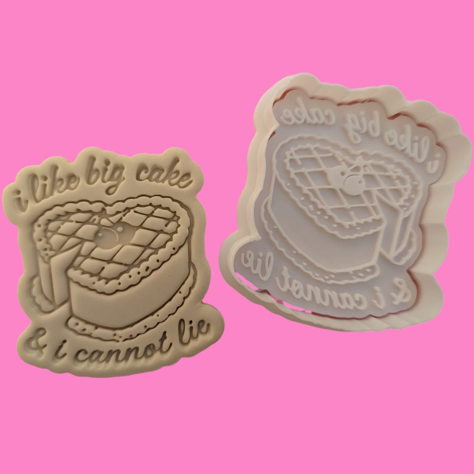 Two cookie cutters with the phrase 'I like big cake I cannot lie' printed on them, one in bold white letters on a dark background, and the other in a beige color.