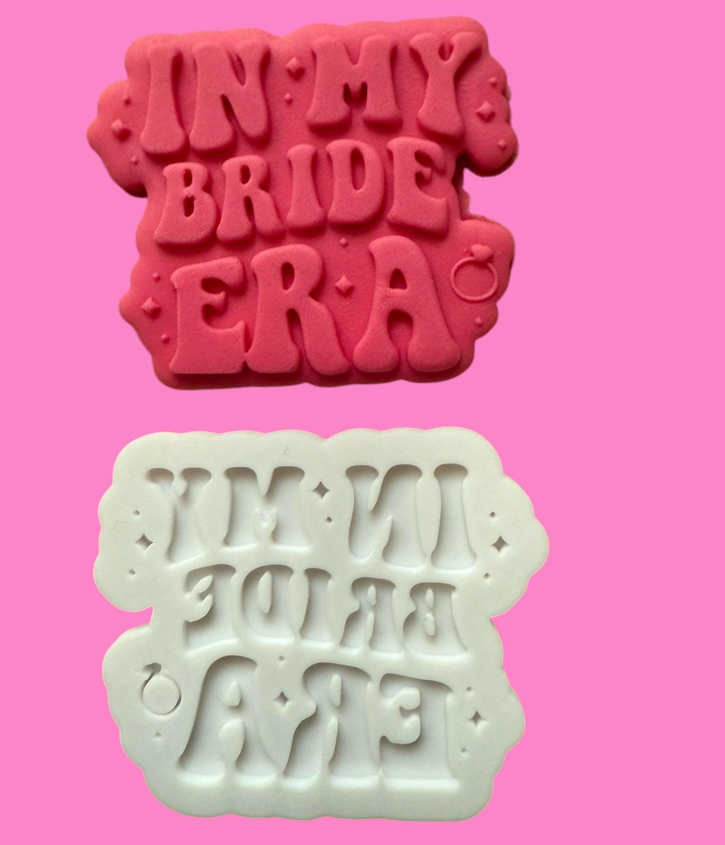 Two cookie cutters with the phrase 'IN MY BRIDE ERA' printed in a trendy font, one in red and one in white, against a pink background.