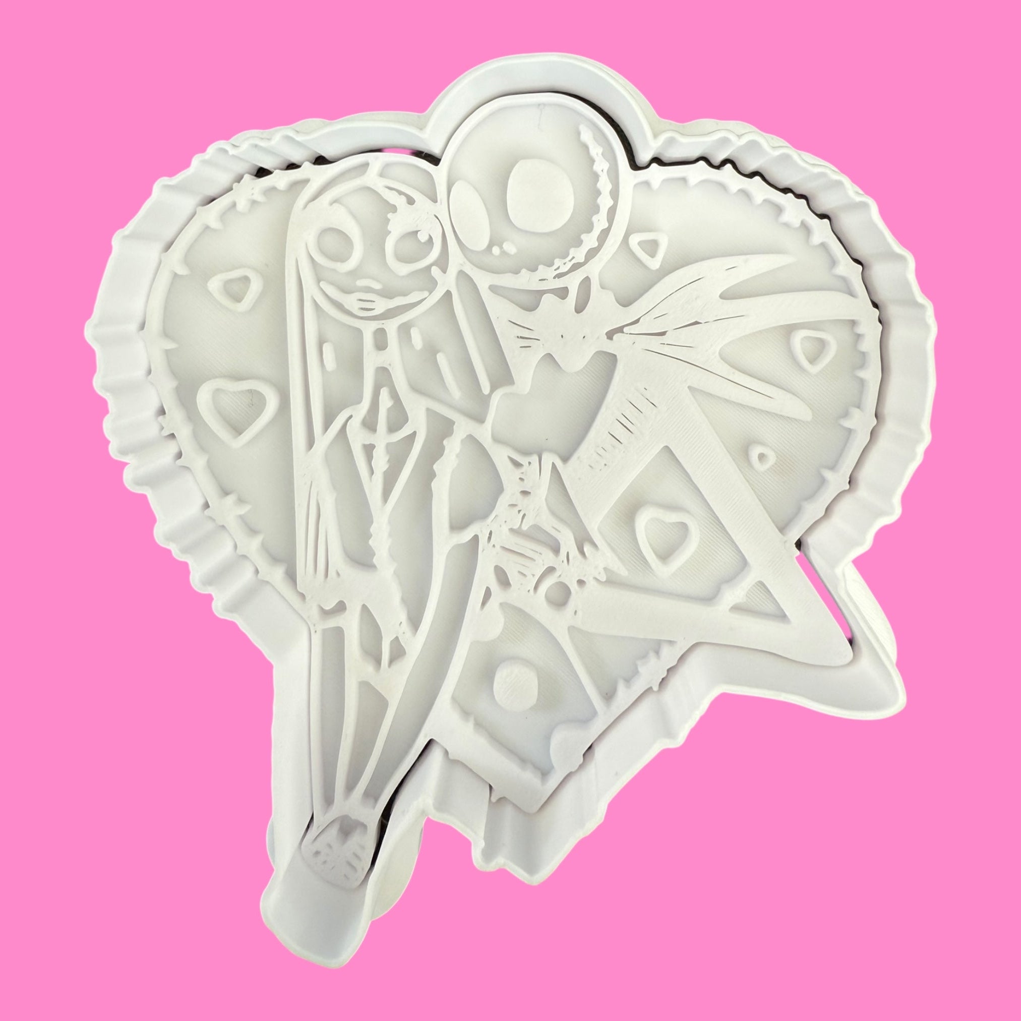 Heart-shaped cookie cutter with decorative design on a pink background