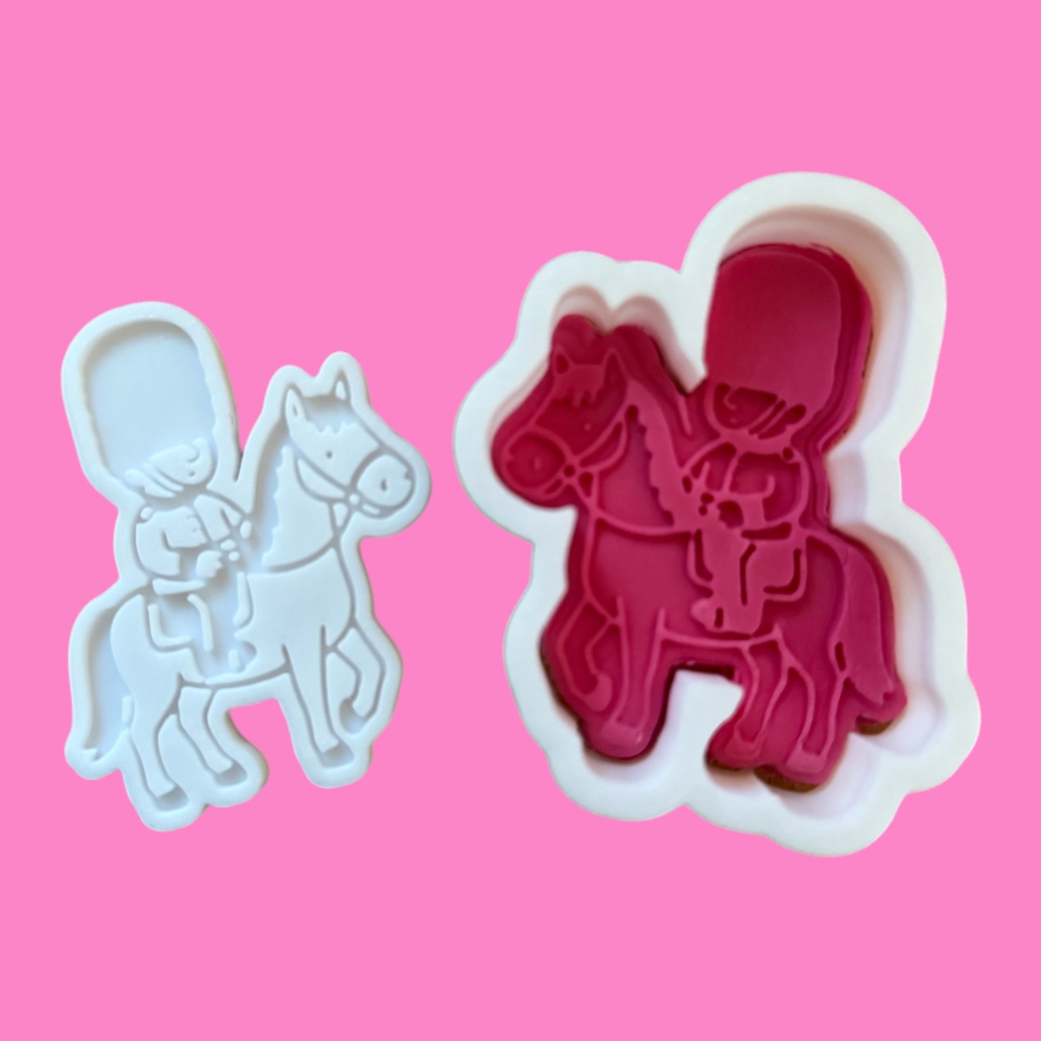 Two cookie cutters in the shape of a mounted guard on horseback, one as a cutter and one as an embosser, displayed on a pink background.