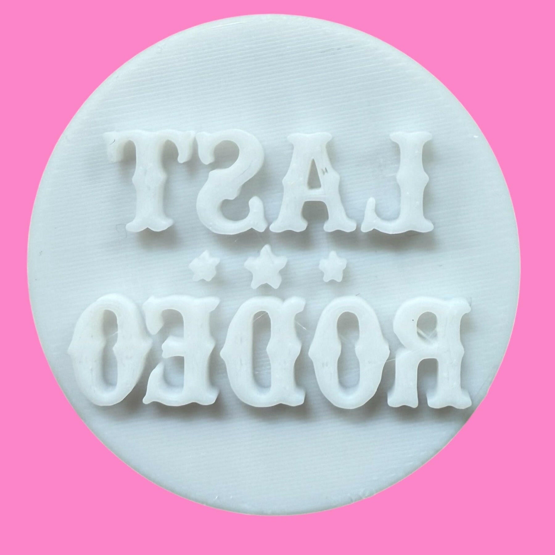 A white cookie cutter and stamp set with the text 'LAST RODEO' in bold western-style font, against a pink background.