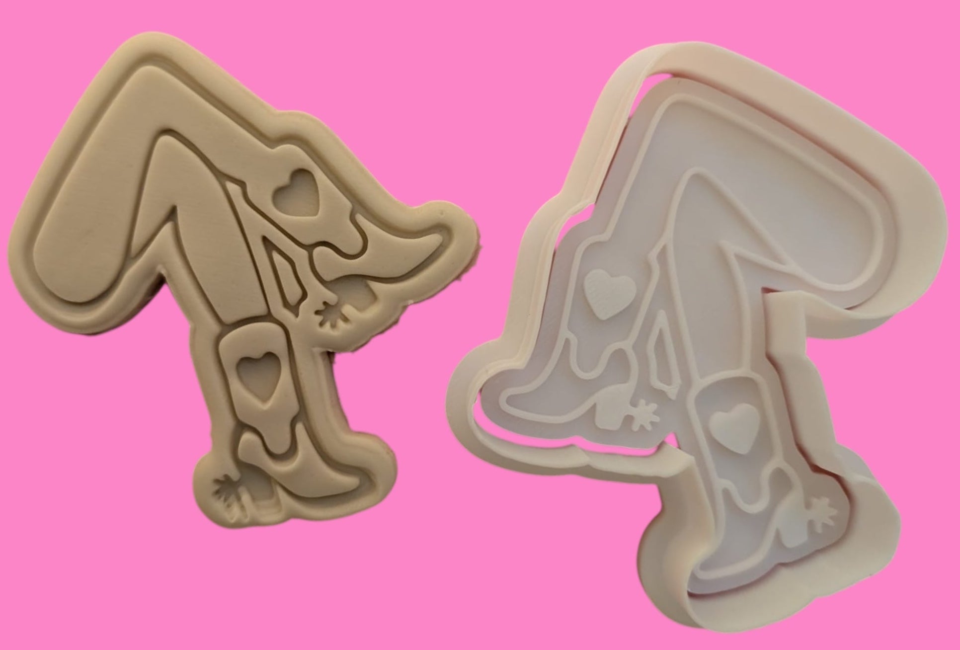 Two cookie cutters in the shape of cowgirl boots and legs with heart details on a pink background.