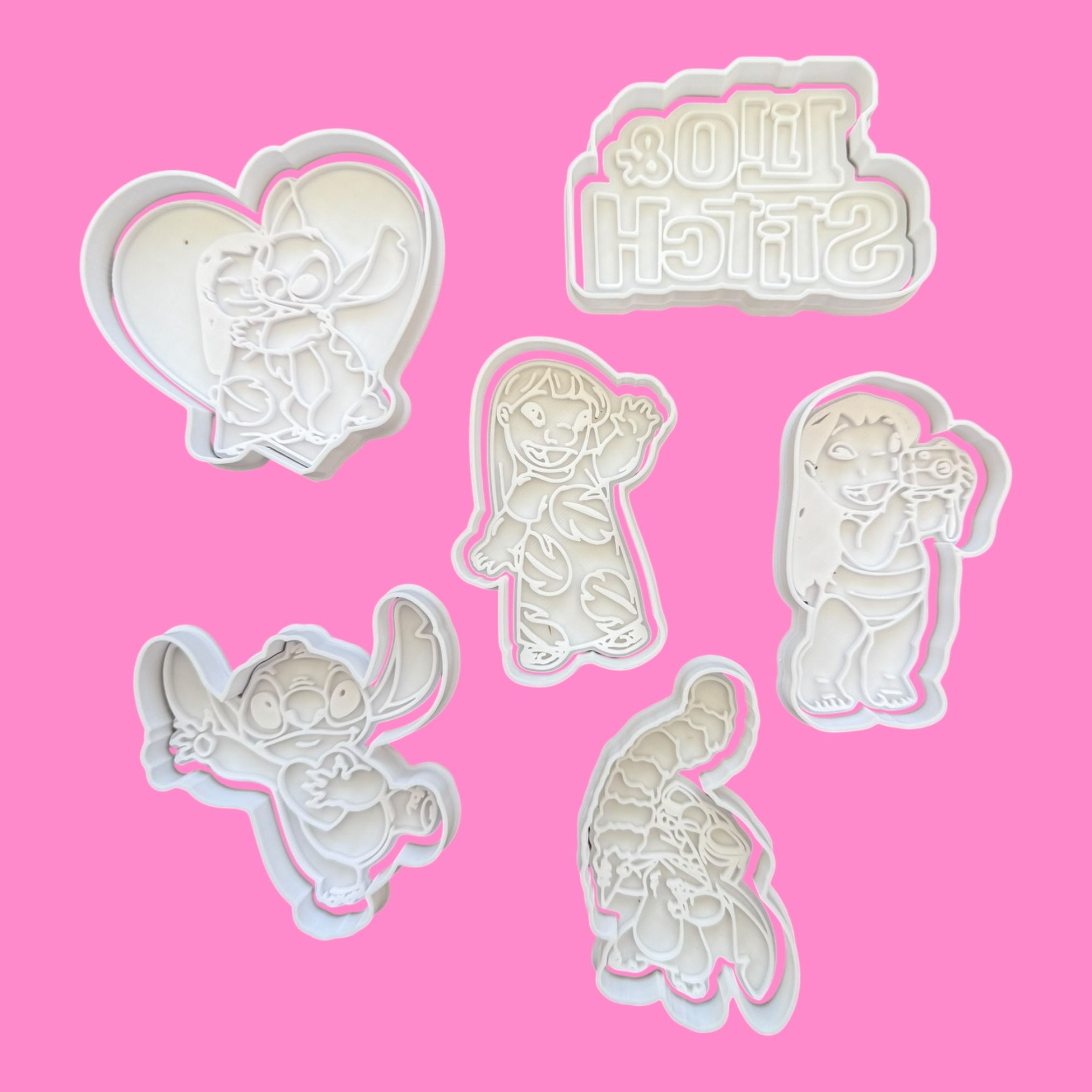 Set of white plastic cookie cutters with cartoon characters on a pink background