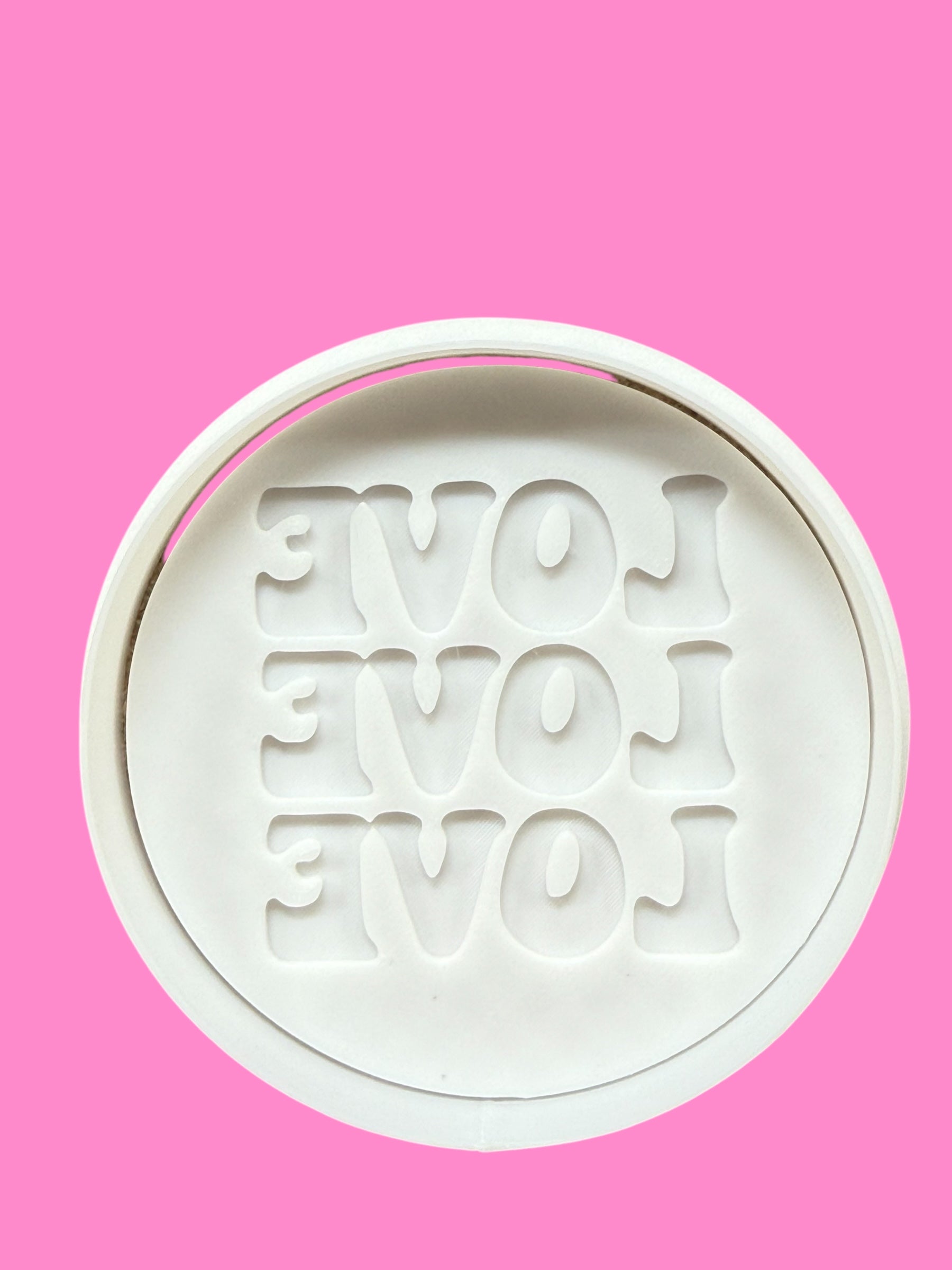 A cookie cutter with the embossed text 'LOVE LOVE LOVE' on a pink background.