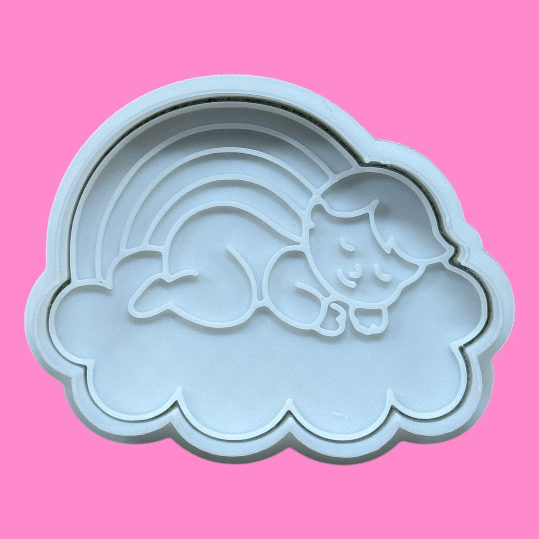 A plastic cookie cutter and embosser in the shape of a sleeping baby on a cloud with a rainbow above.