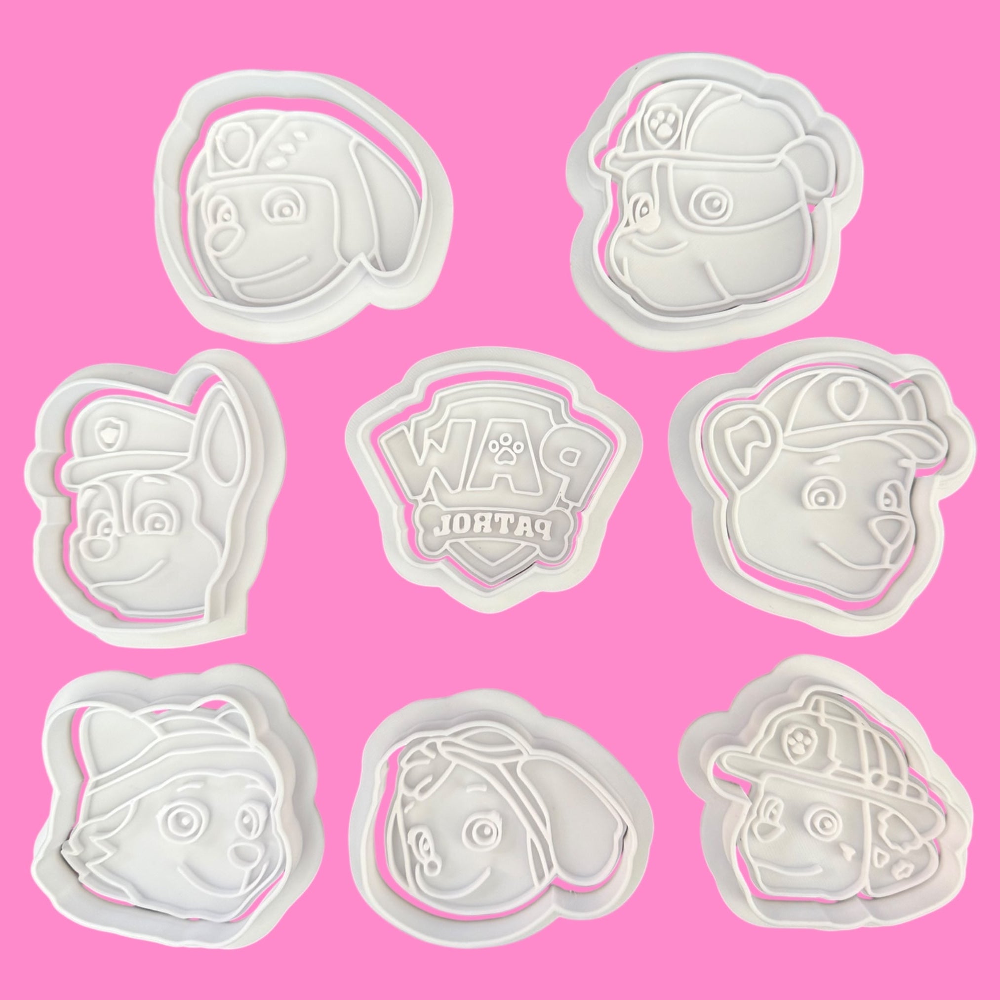 Set of cookie cutters with cartoon character designs on a pink background