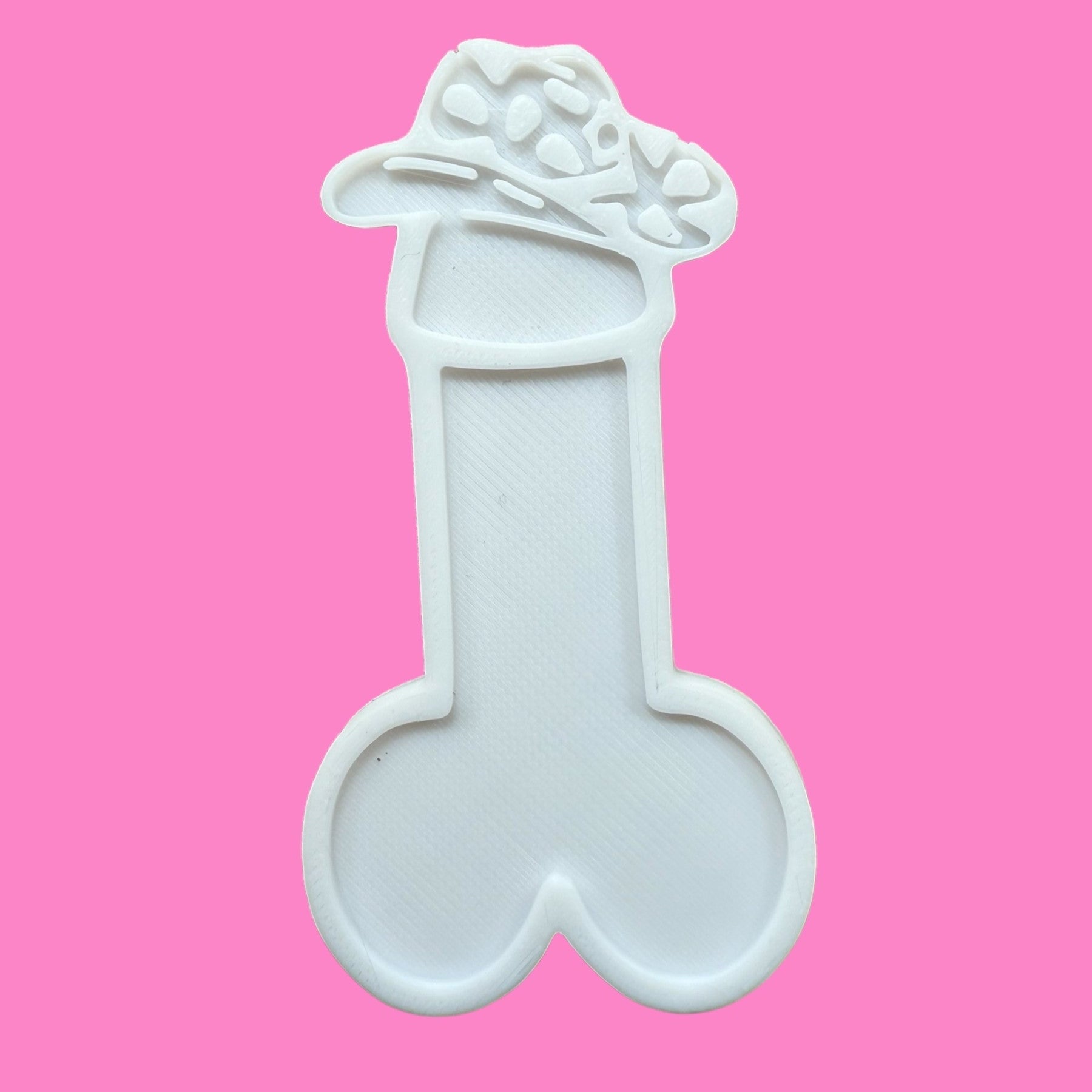 A cookie cutter with a phallic shape, wearing a cowboy hat, on a pink background.