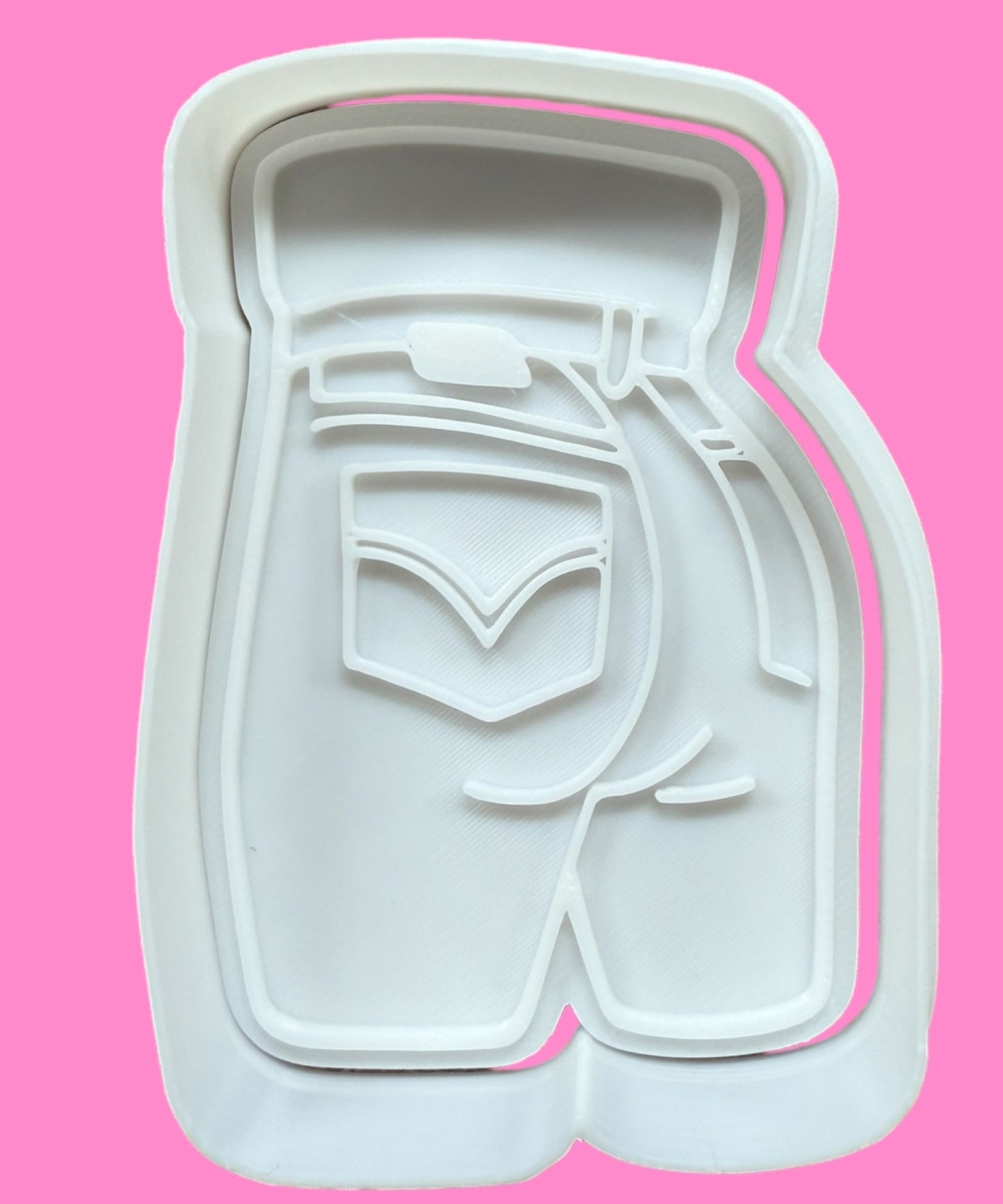 A white, denim-clad buttocks-shaped cookie cutter against a pink background.
