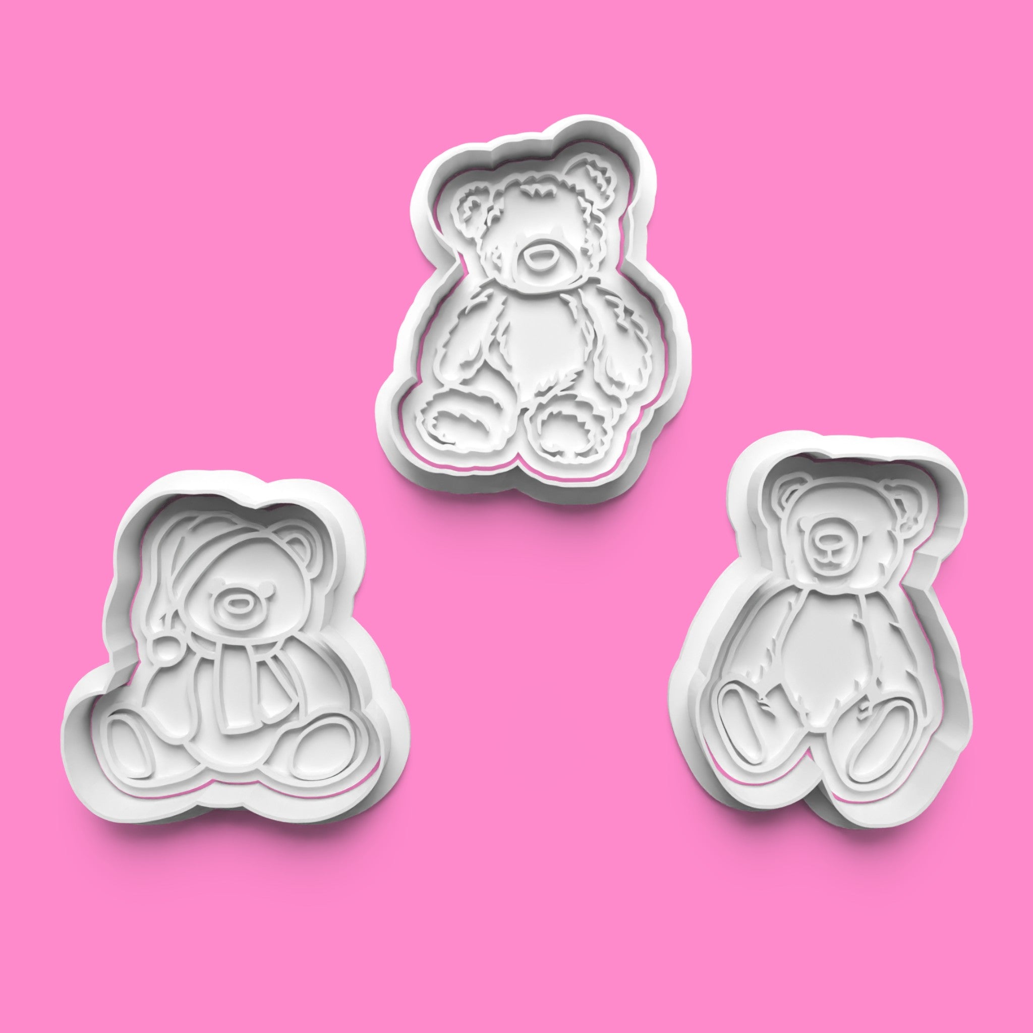 Three white teddy bear-shaped cookie cutters on a pink background.