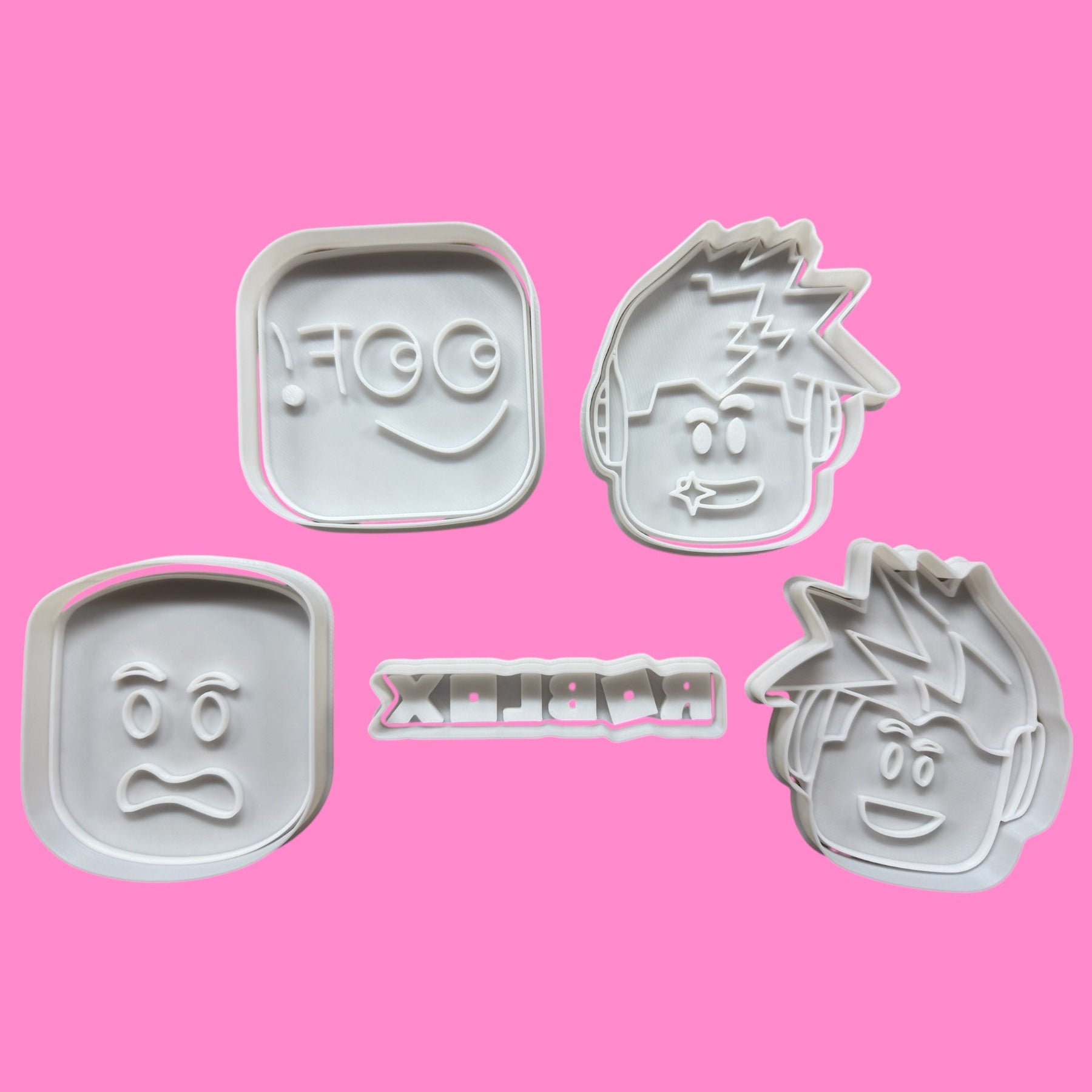 A collection of five Roblox-inspired cookie cutters and embossers, featuring the iconic logo and four character designs, placed against a pink background.