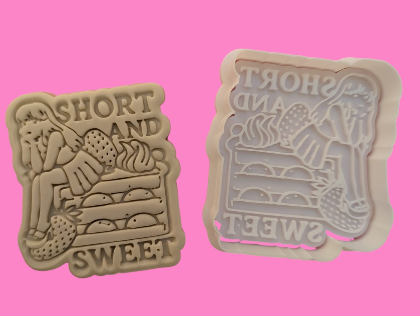 Two cookie cutters with embossed designs, one with the phrase 'Short and Sweet' and the other resembling a stacked outfit, both in pink color.