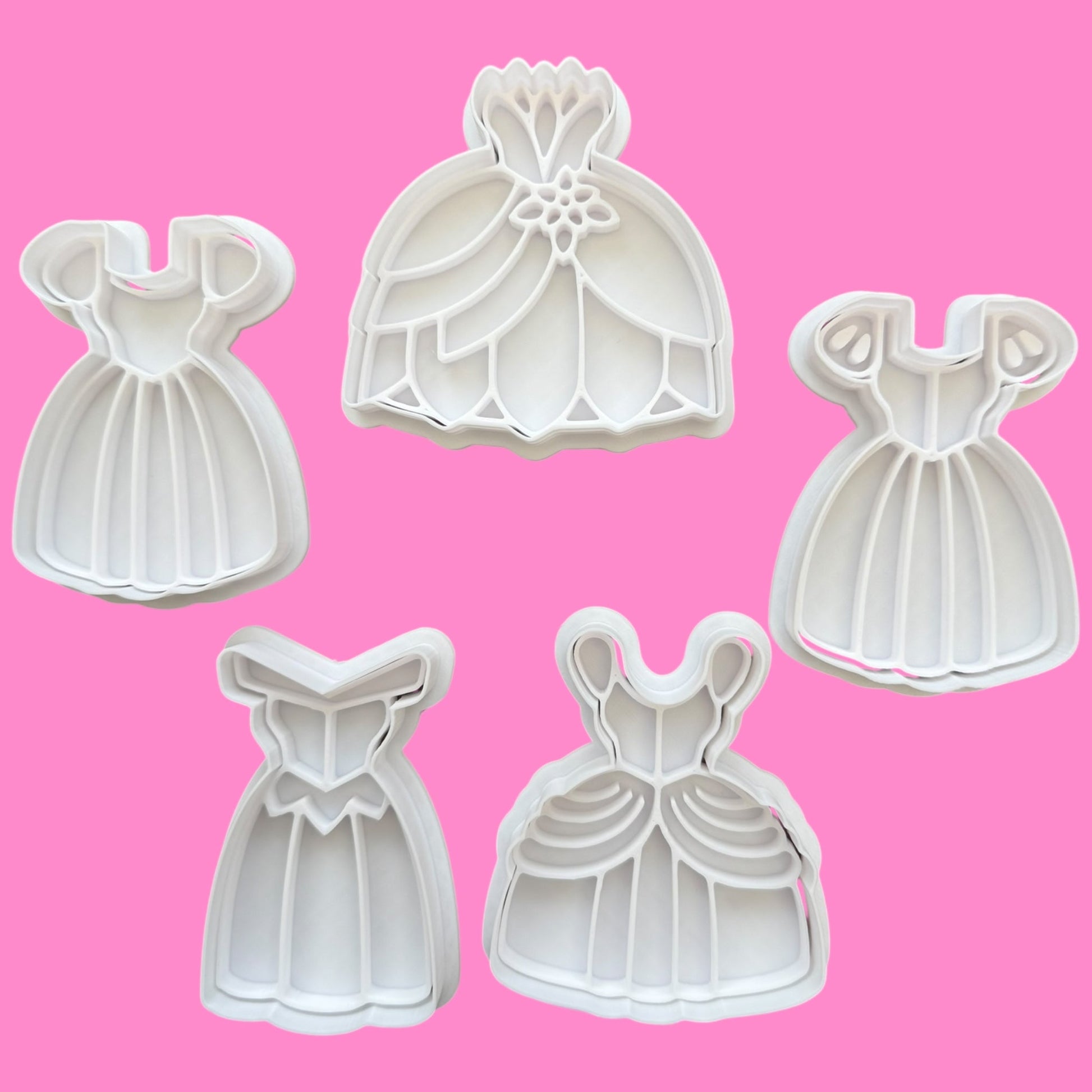 Set of five dress-shaped cookie cutters on a pink background