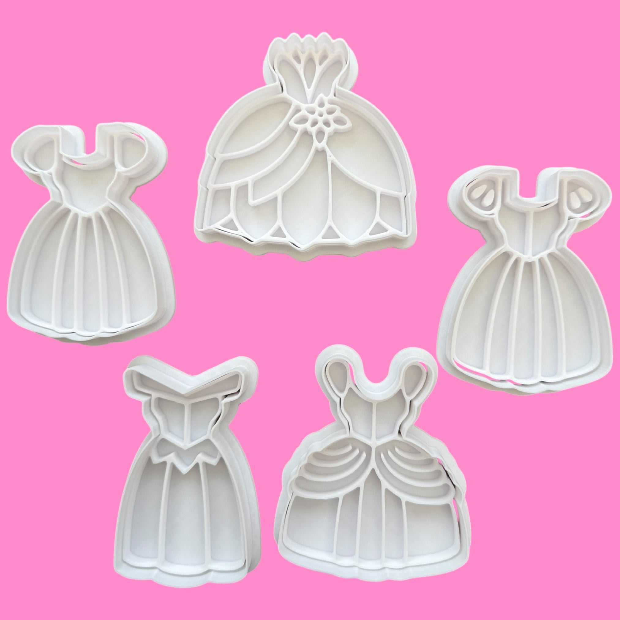 Set of five dress-shaped cookie cutters on a pink background