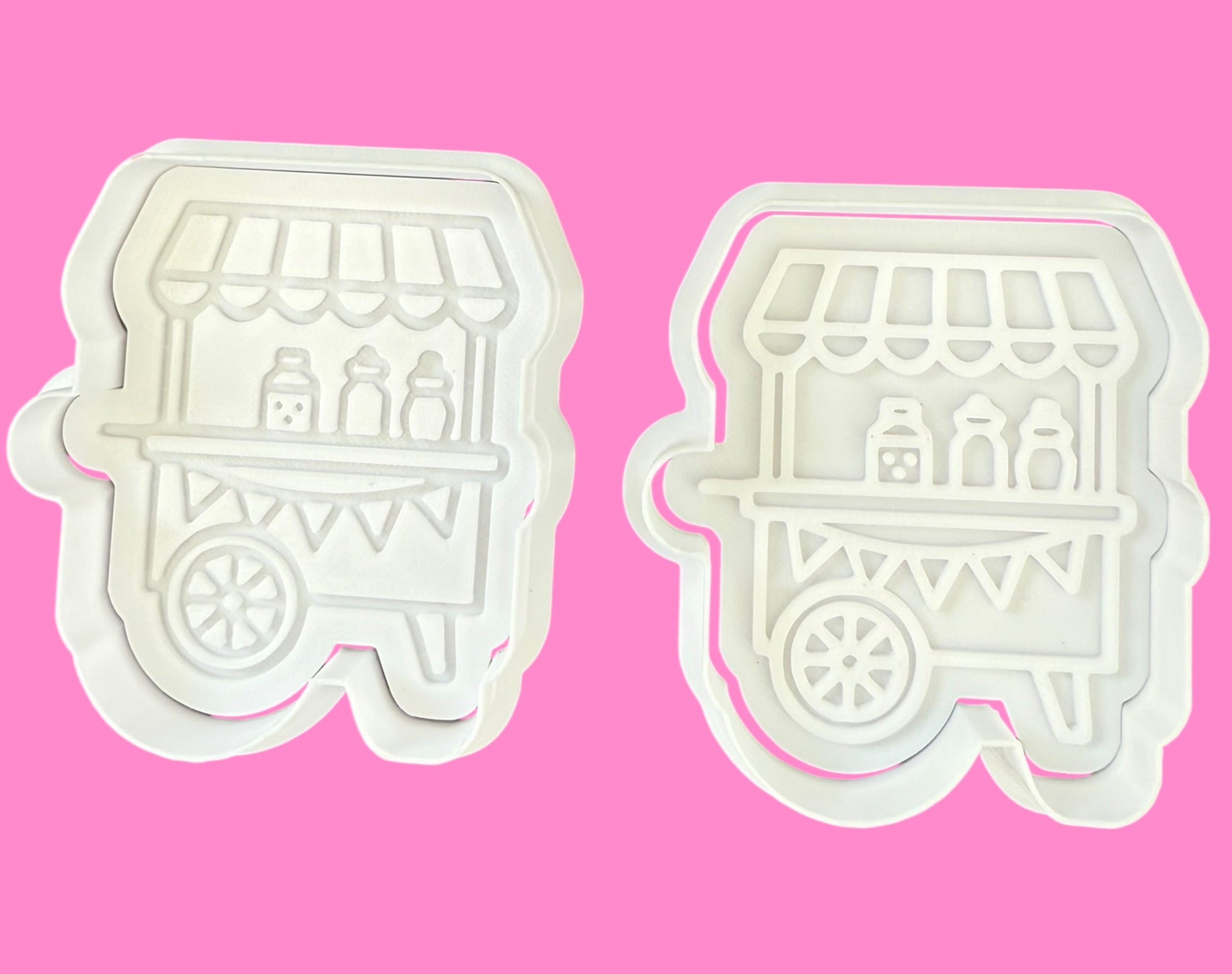Two white cookie cutters shaped like vintage carts on a pink background