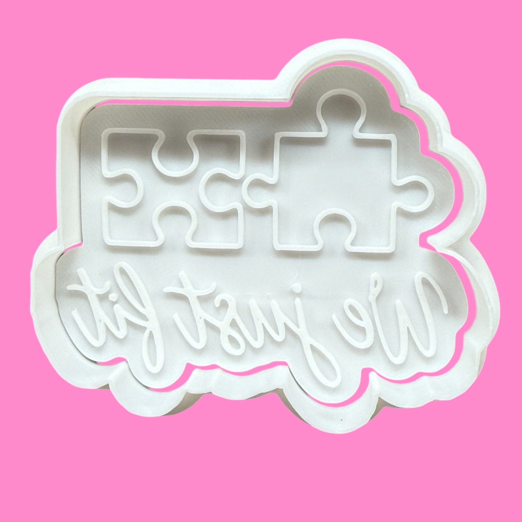 A white plastic cookie cutter and embosser with a jigsaw puzzle design and the phrase 'We Just Fit' engraved on it.