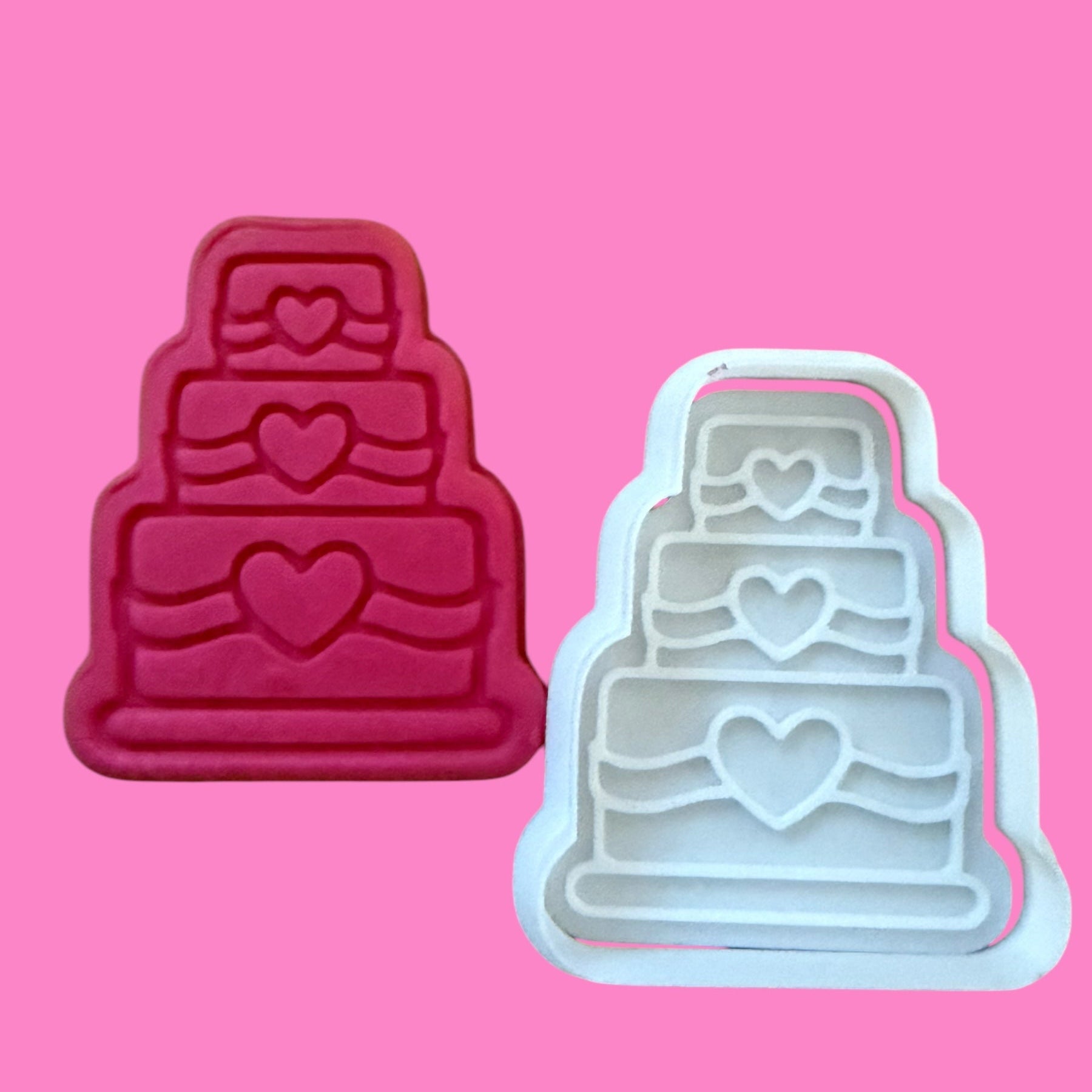 Two cake-shaped cookie cutters on a pink background