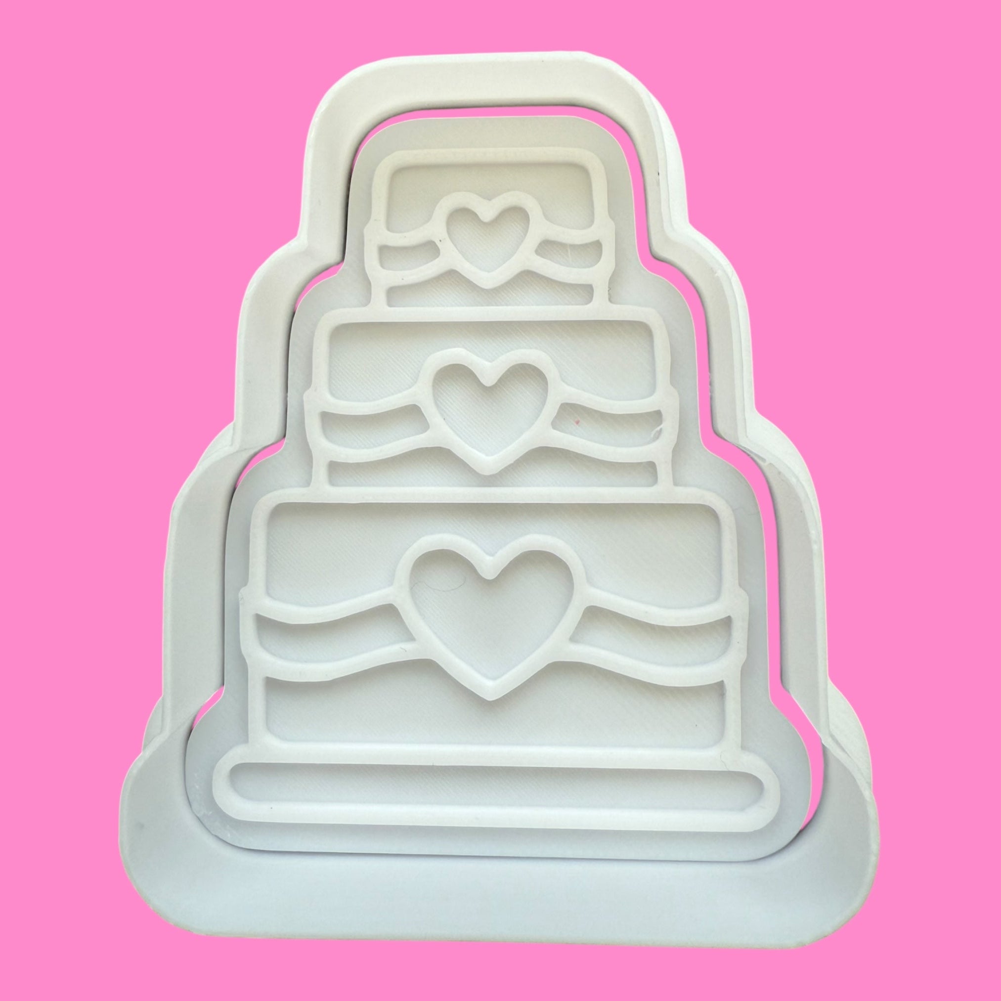White plastic mold shaped like a tiered cake with heart designs on a pink background